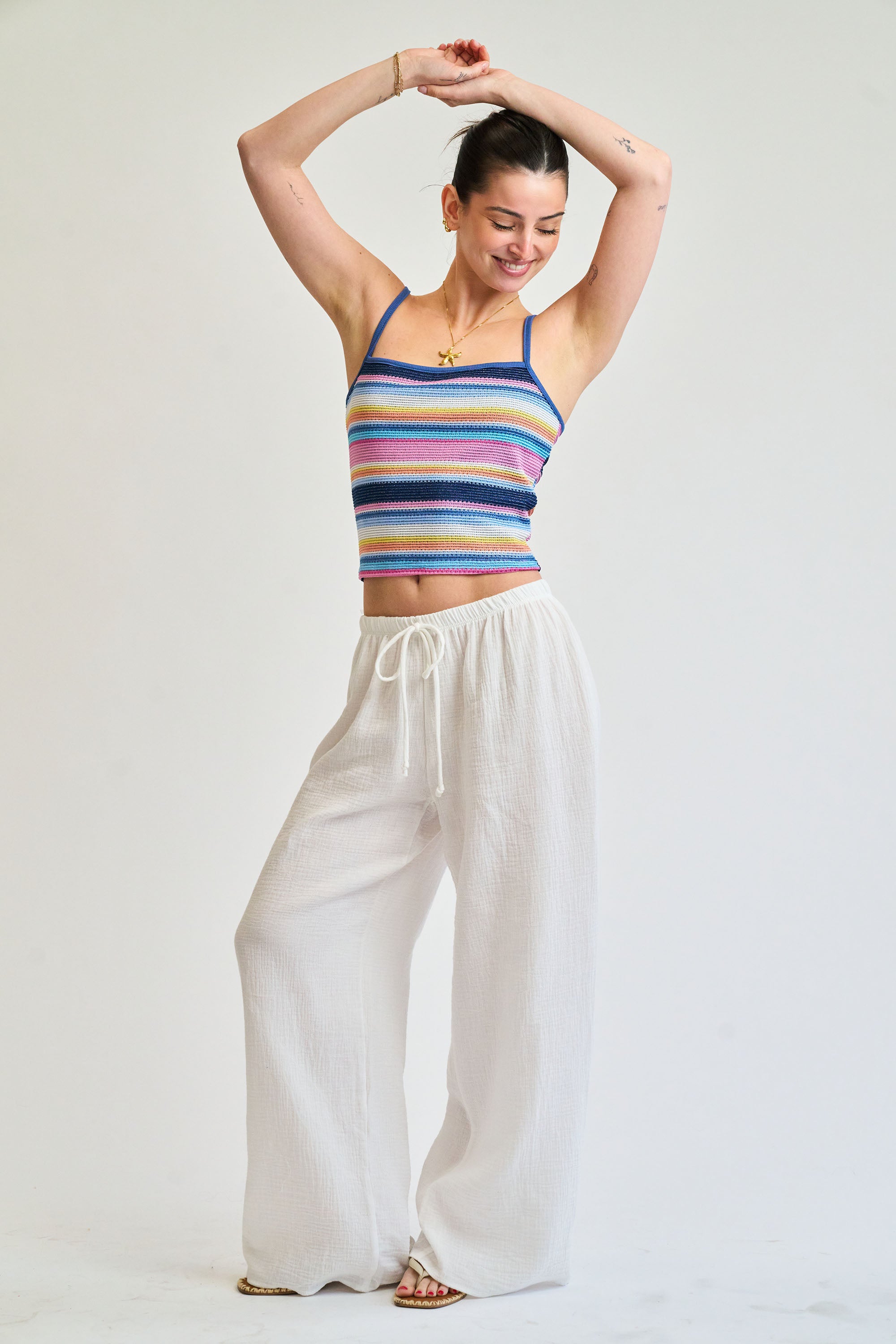 Woman wearing a colorful striped tank top and white pants on a plain background