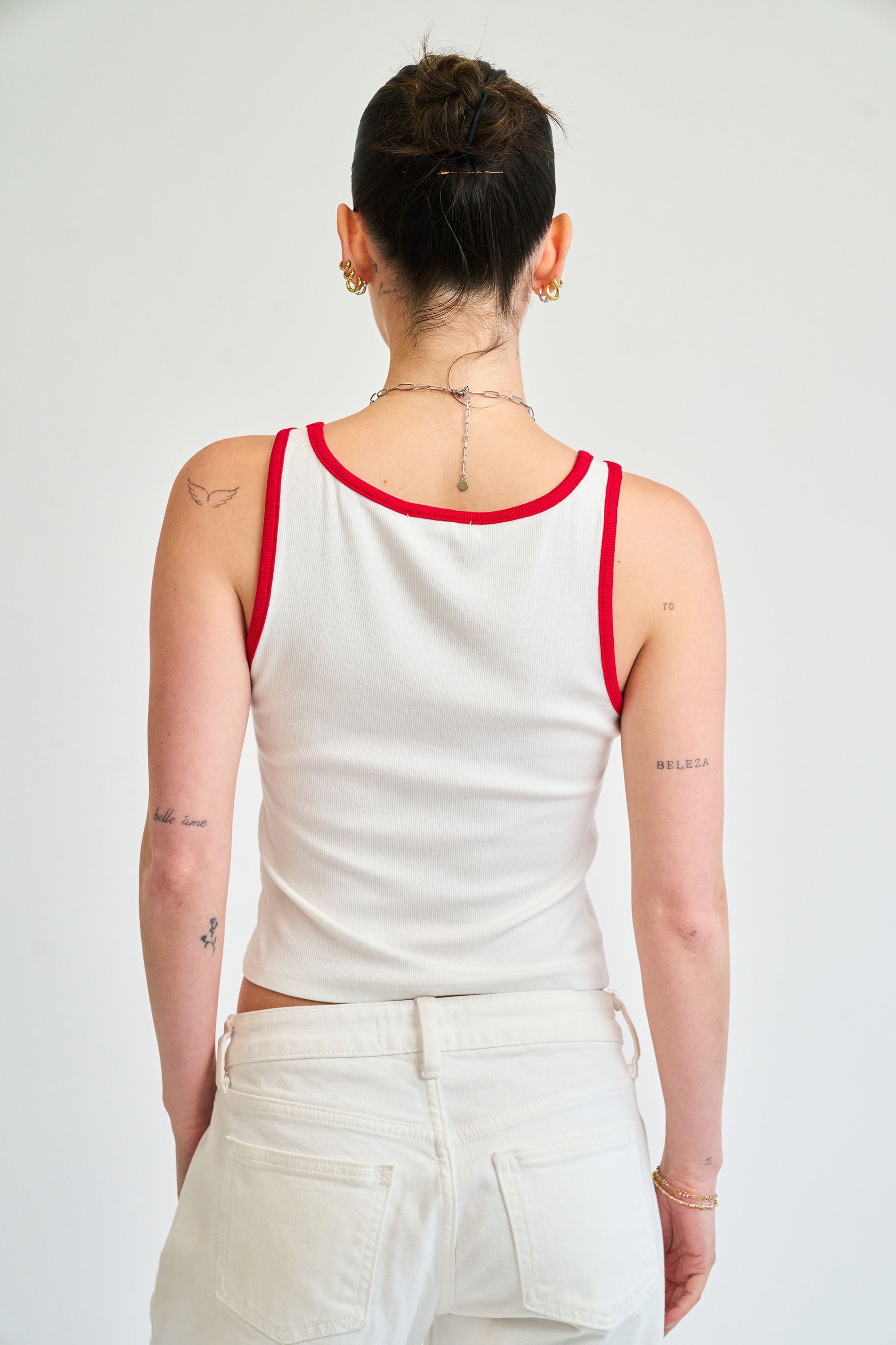 Person wearing a white tank top with red trim on a plain background
