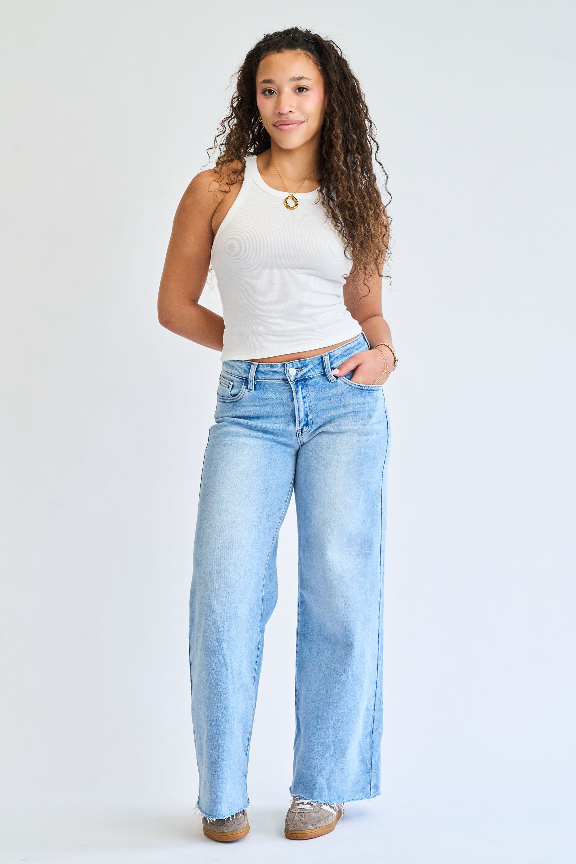Woman wearing a white tank top and light blue jeans on a plain background