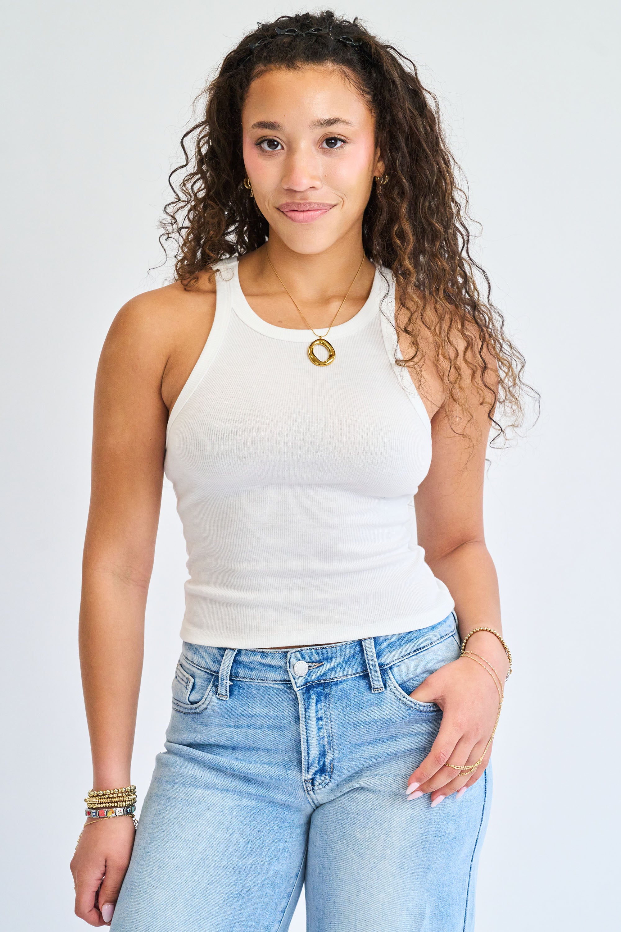 Woman wearing a white tank top and light blue jeans against a plain background