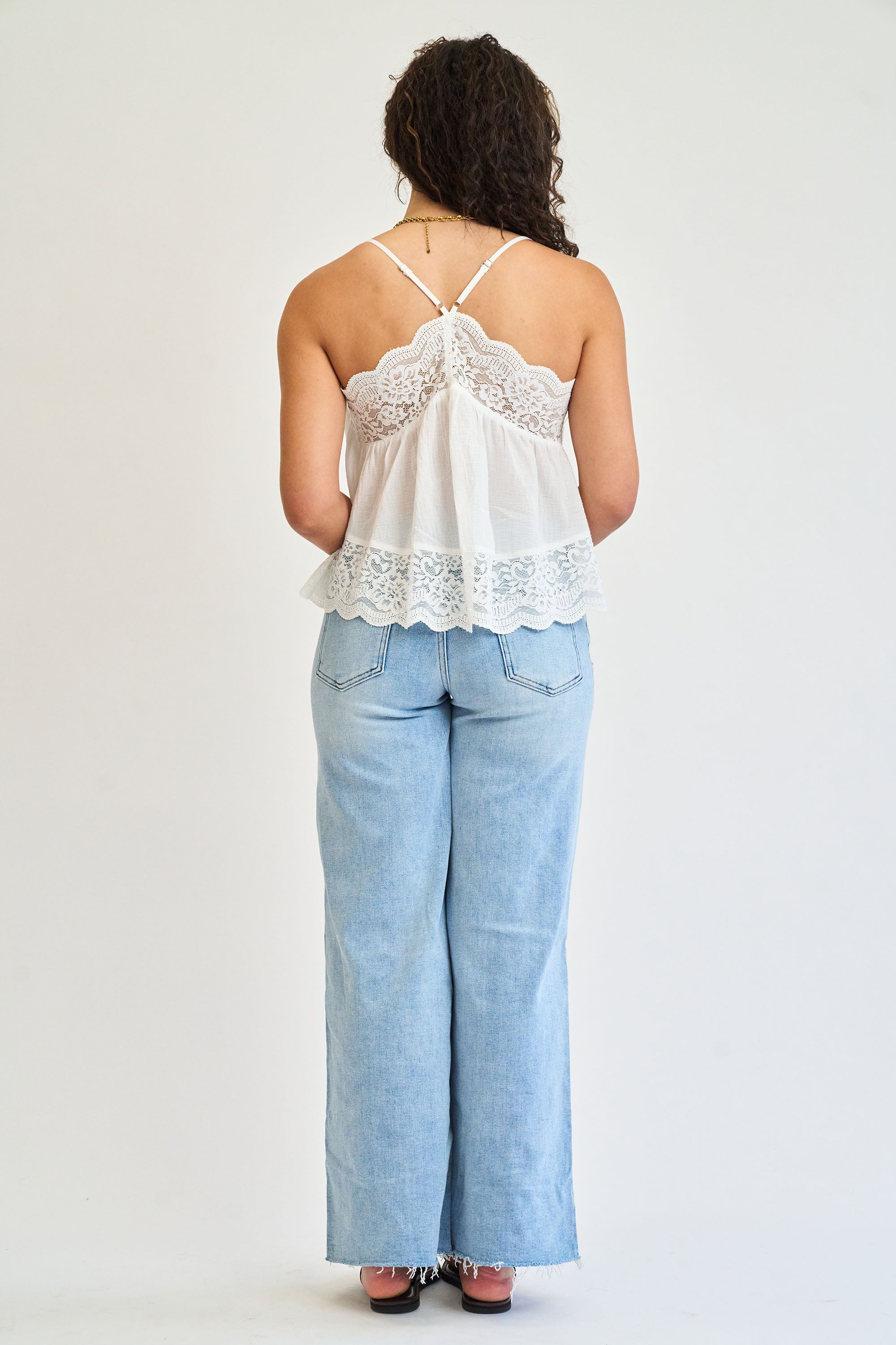 Person wearing a white lace top and light blue jeans on a plain background