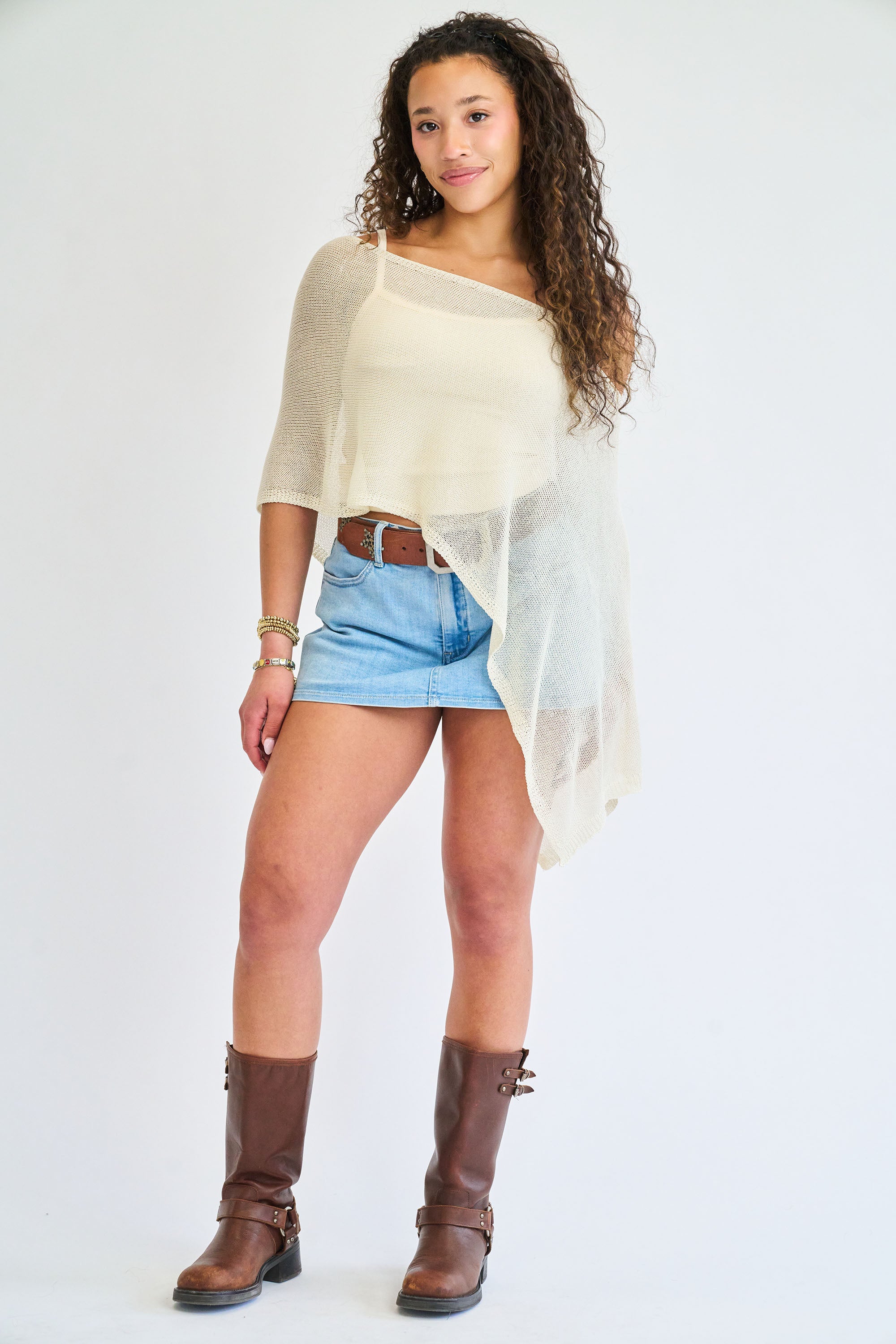 Woman wearing a beige top, denim shorts, and brown boots on a white background