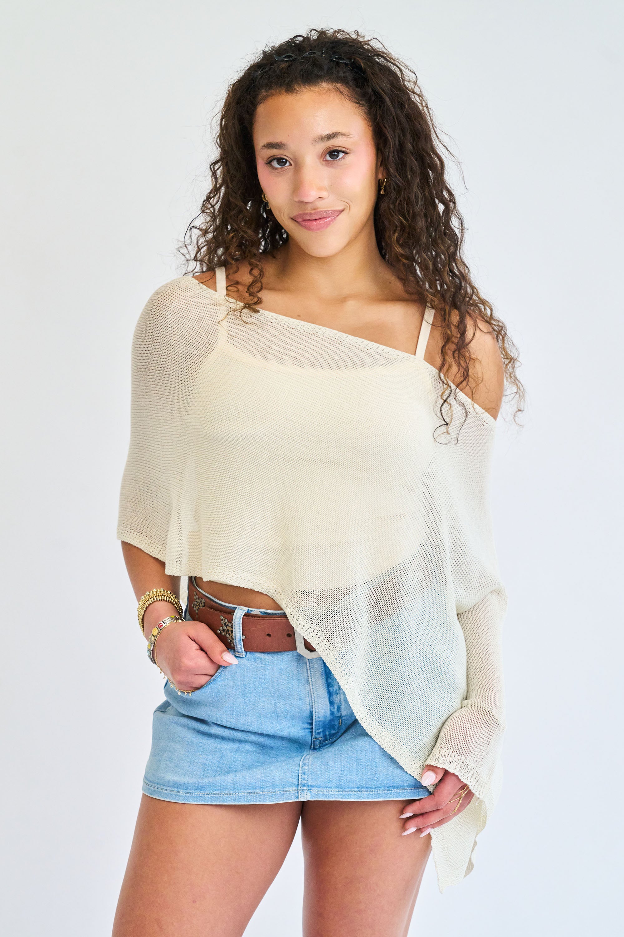 Woman wearing a light-colored off-shoulder top and denim shorts on a white background