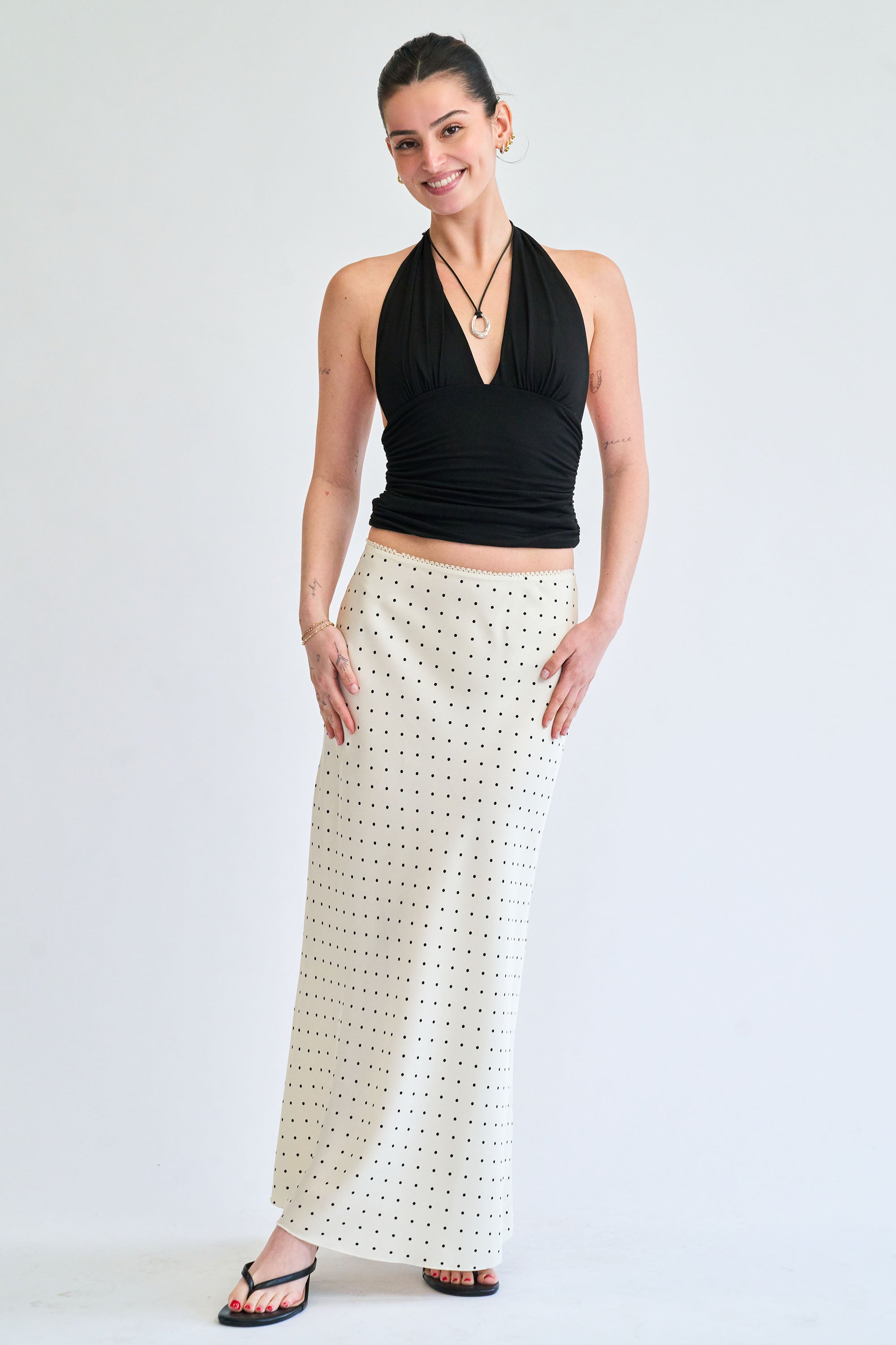 Woman wearing a black halter top and white patterned skirt on a white background