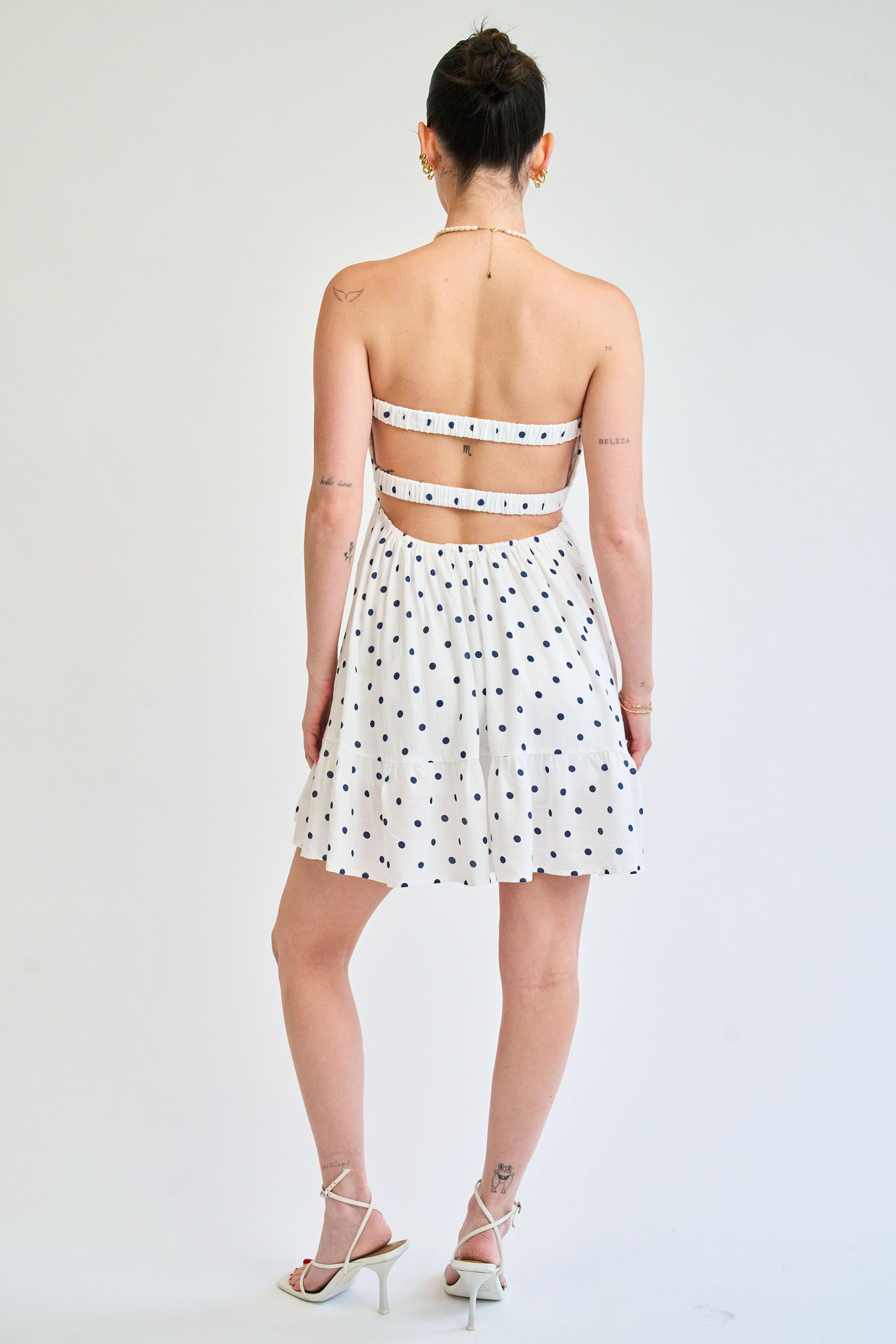Woman wearing a white dress with black polka dots on a plain background