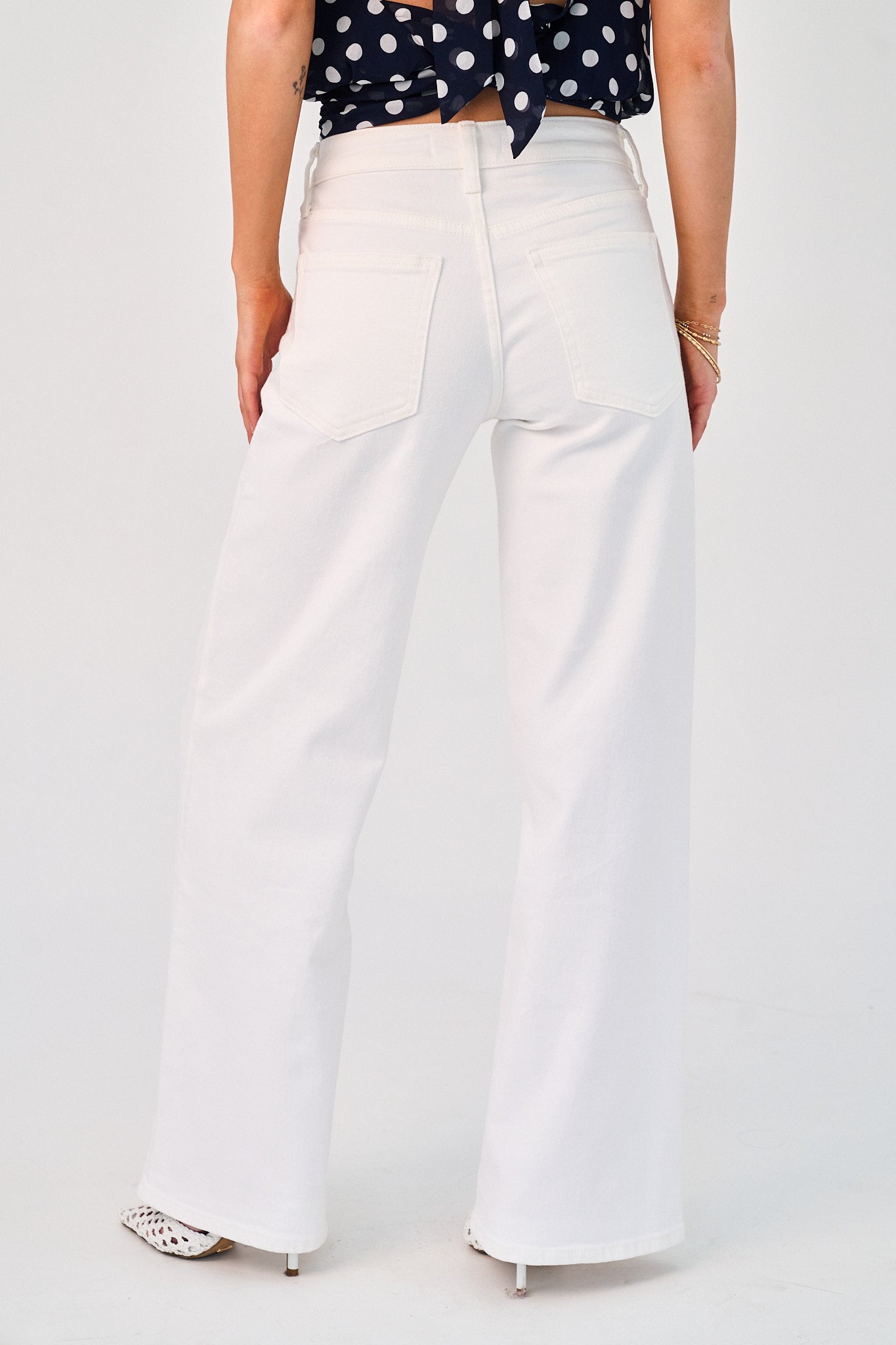 Person wearing white wide-leg pants with a navy polka dot top on a light gray background