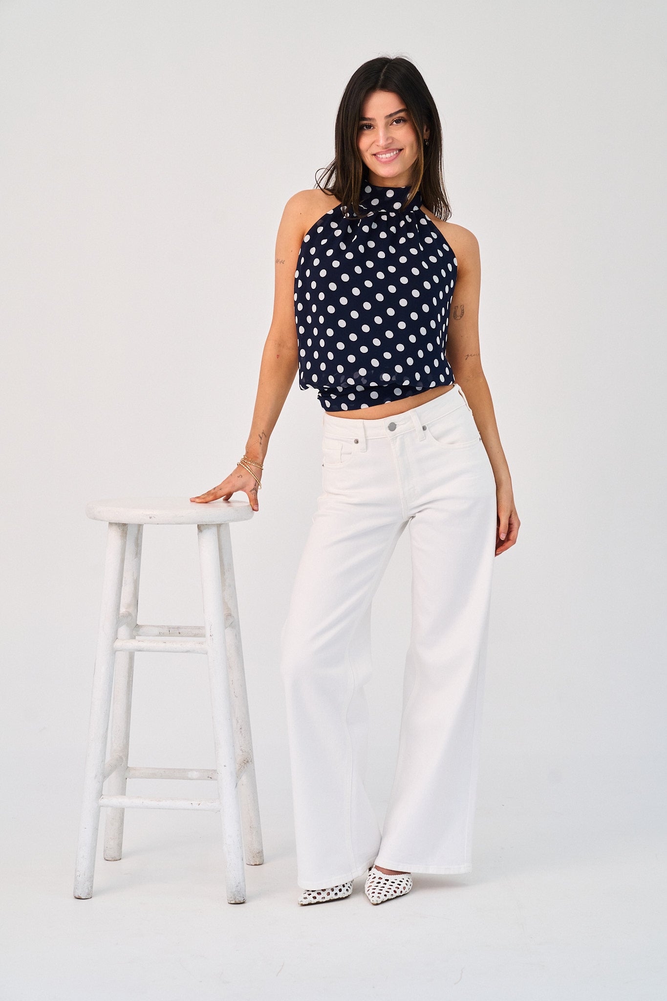 Woman wearing a black and white polka dot top and white pants on a white background