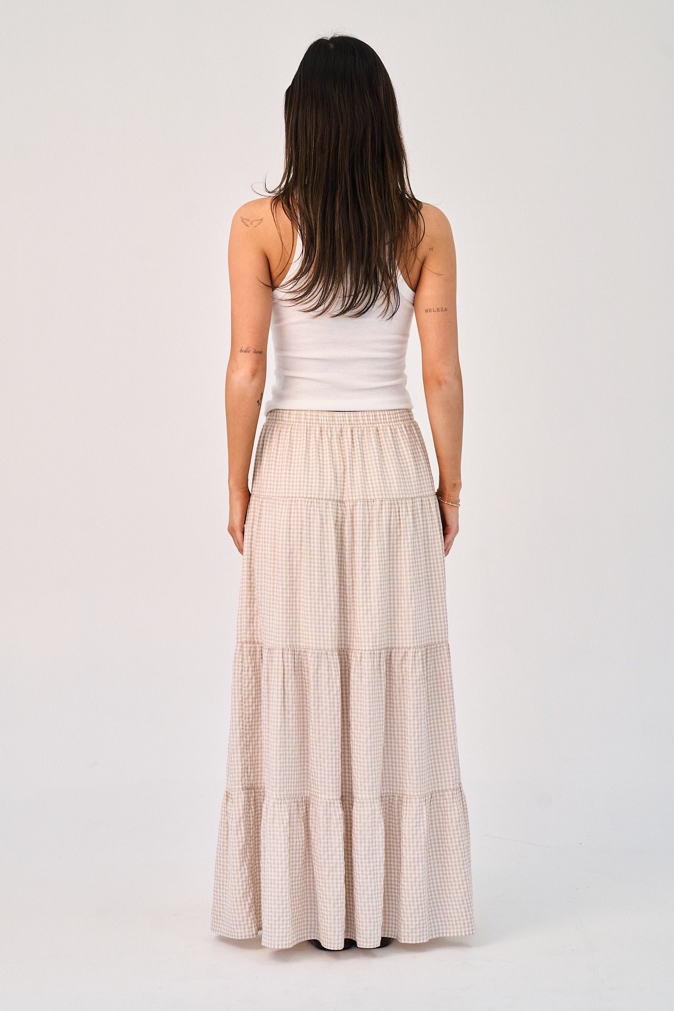 Woman wearing a white top and beige tiered skirt on a white background