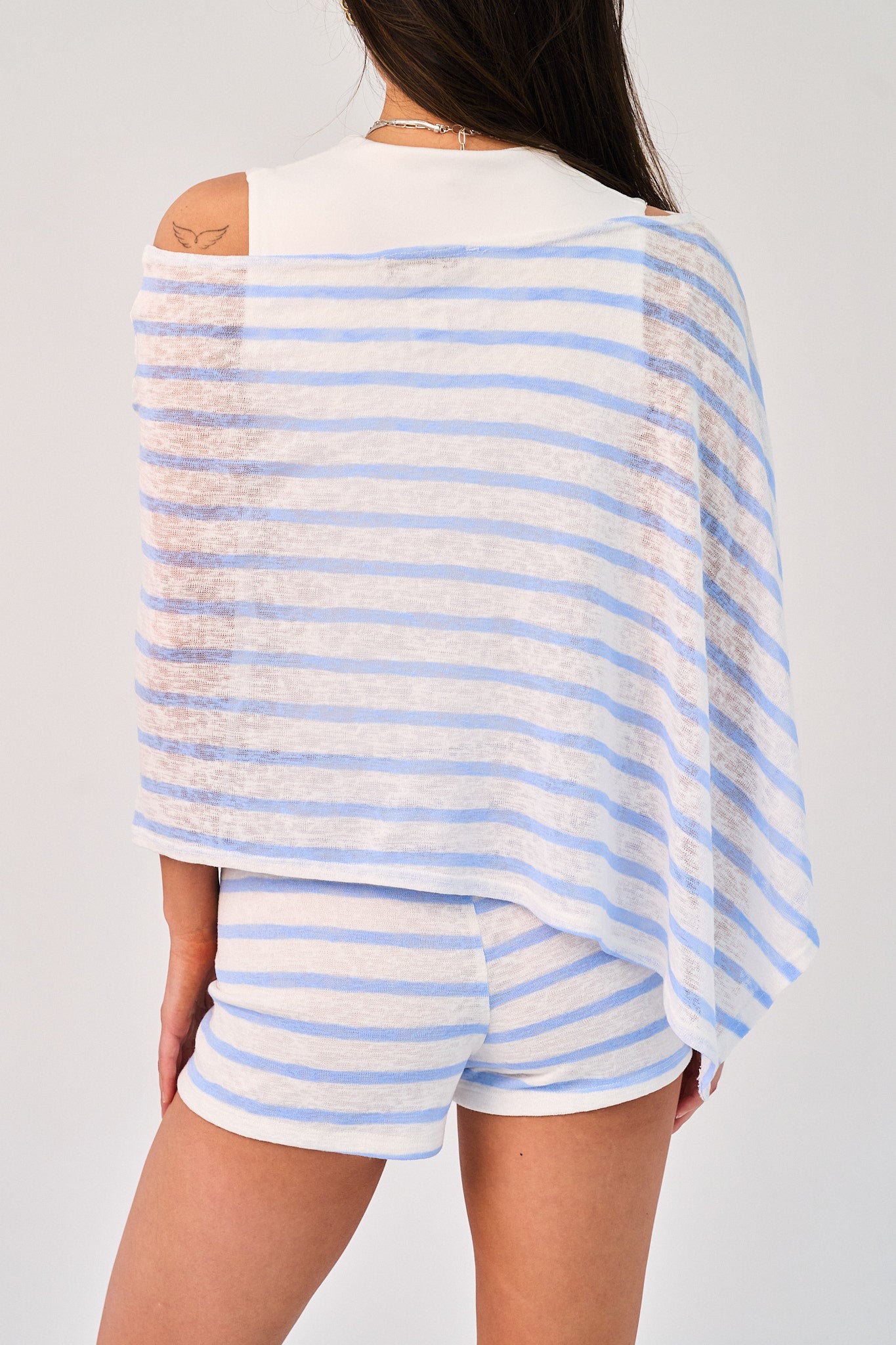 Person wearing a blue and white striped poncho and shorts on a plain background