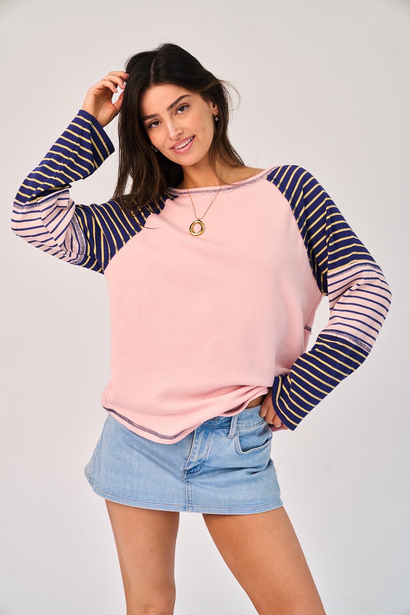 Woman wearing a pink and navy striped long-sleeve top with denim shorts on a plain background
