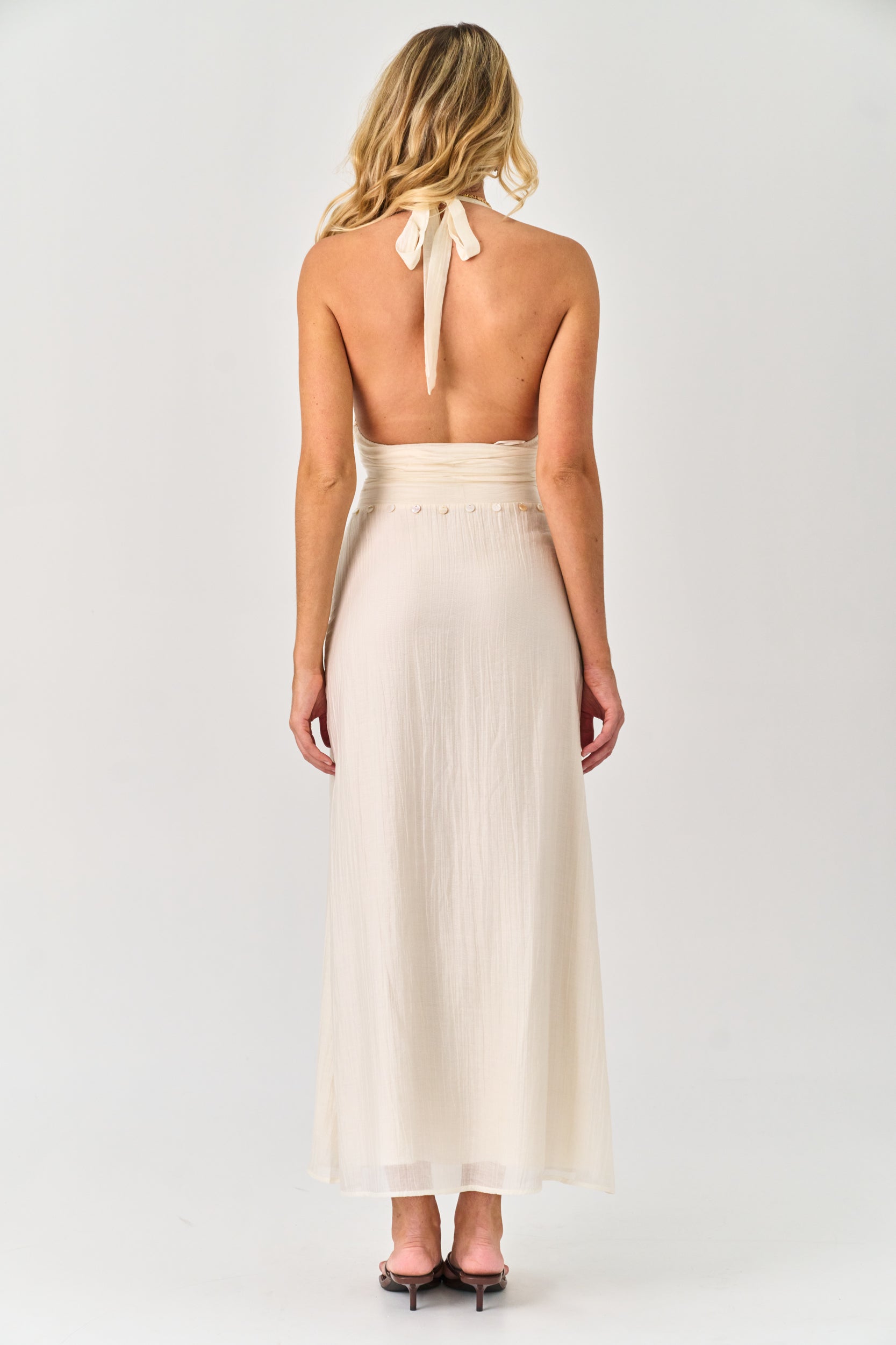 Woman wearing a long, light-colored dress with a halter neck design on a white background