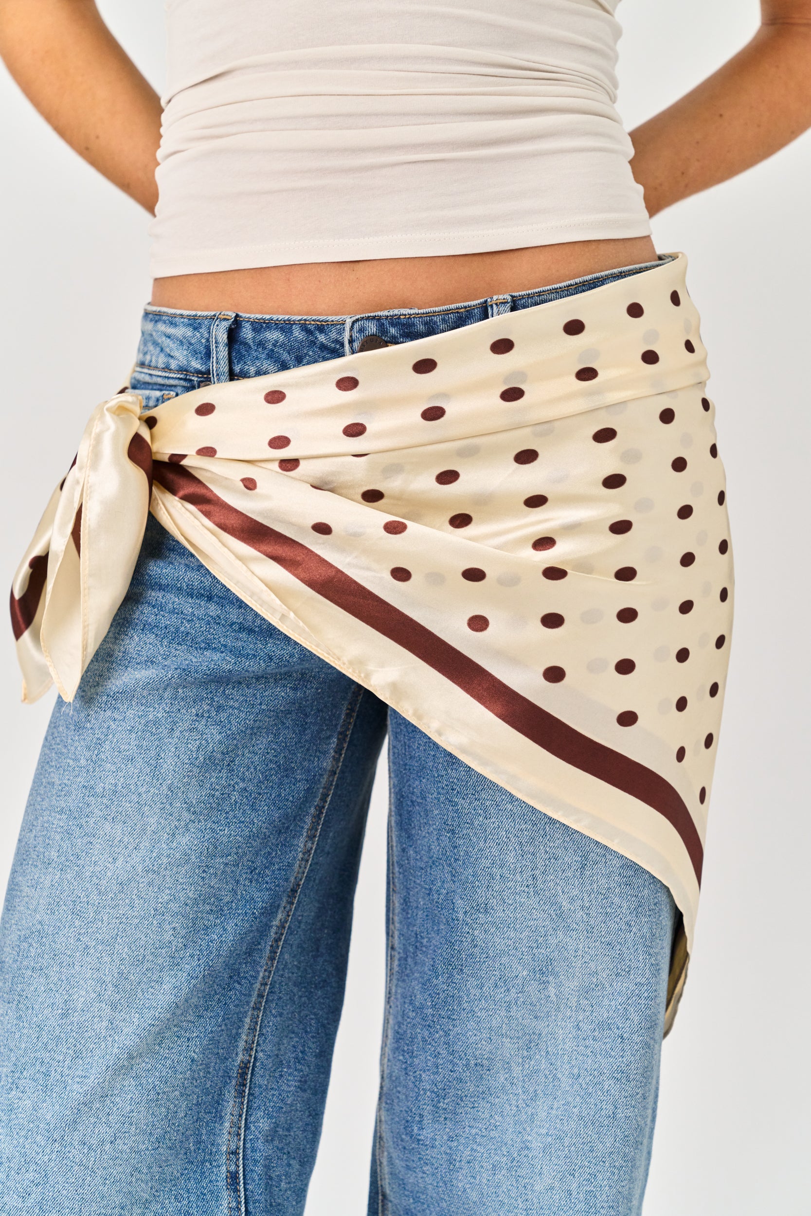 Person wearing a polka dot scarf over jeans on a plain background