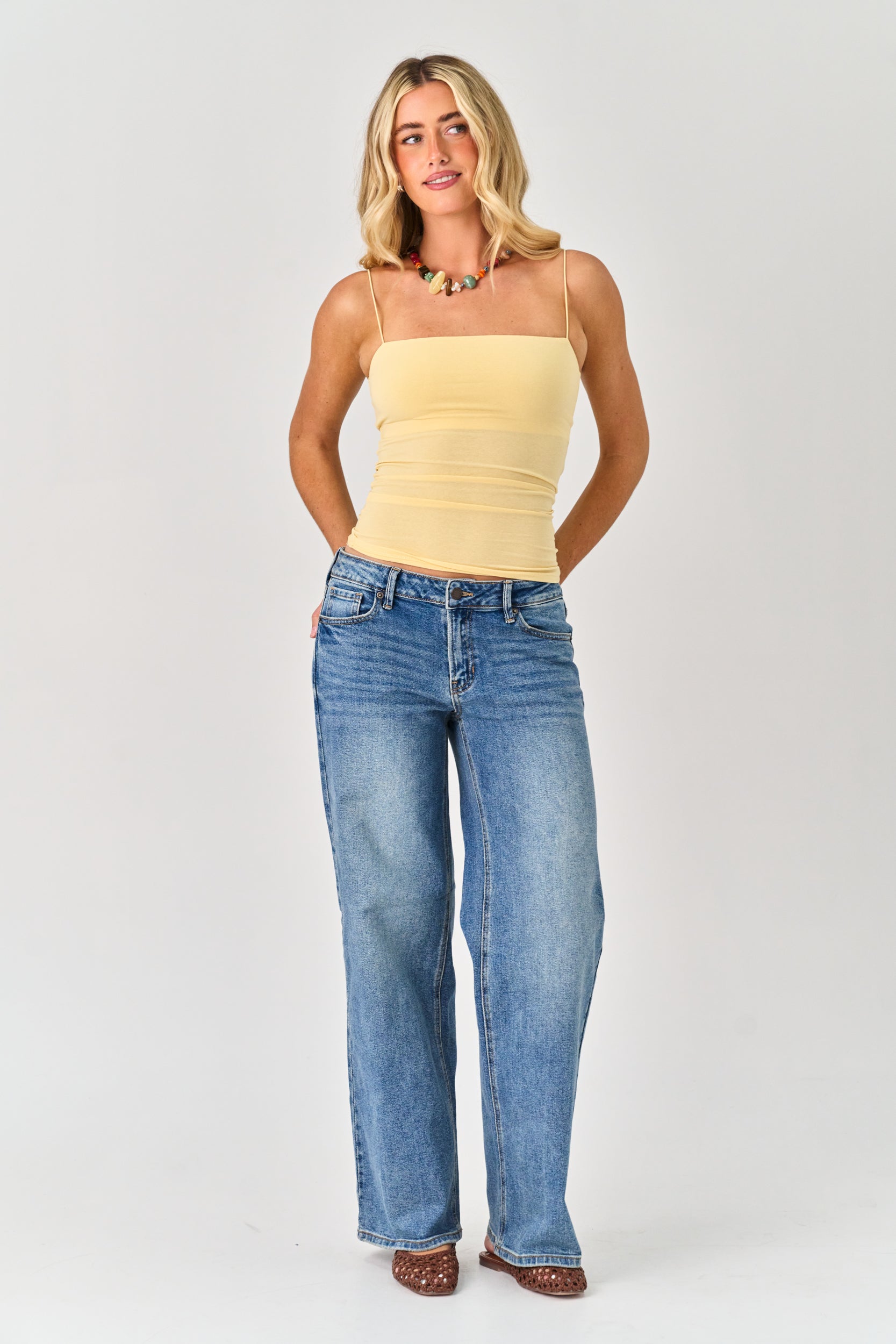 Woman wearing a yellow strapless top and blue jeans on a white background