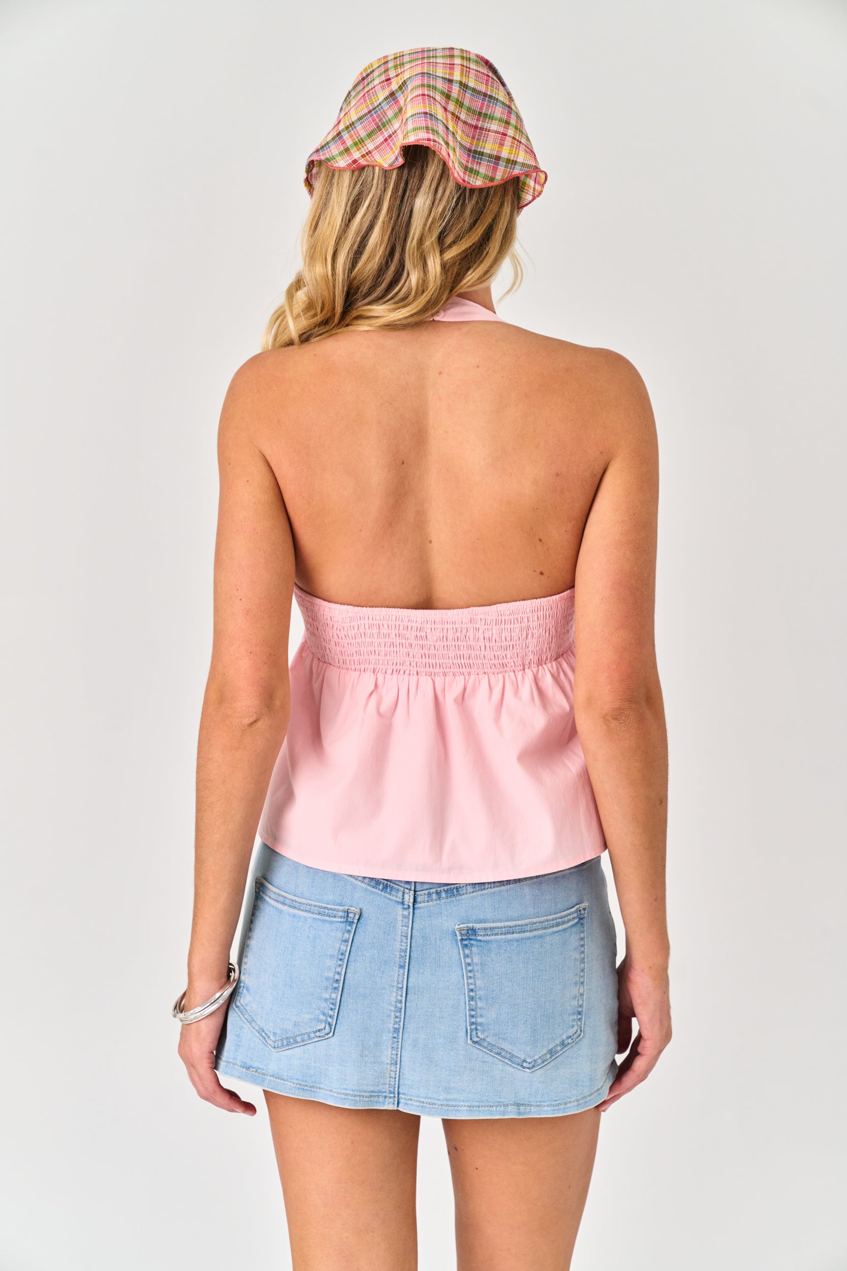 Woman wearing a pink strapless top and denim skirt with a plaid hat on a white background
