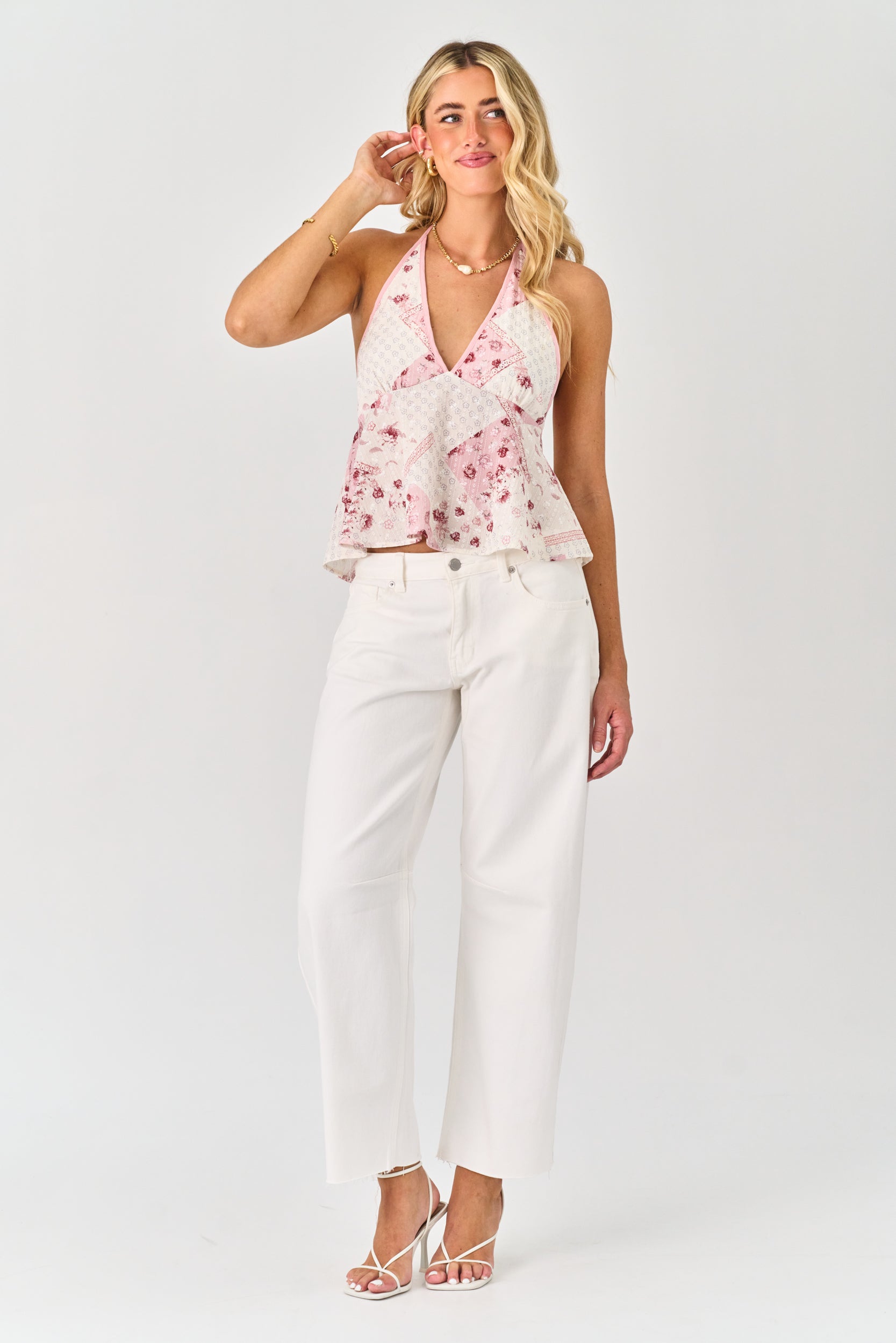Woman wearing a floral top and white pants on a plain background