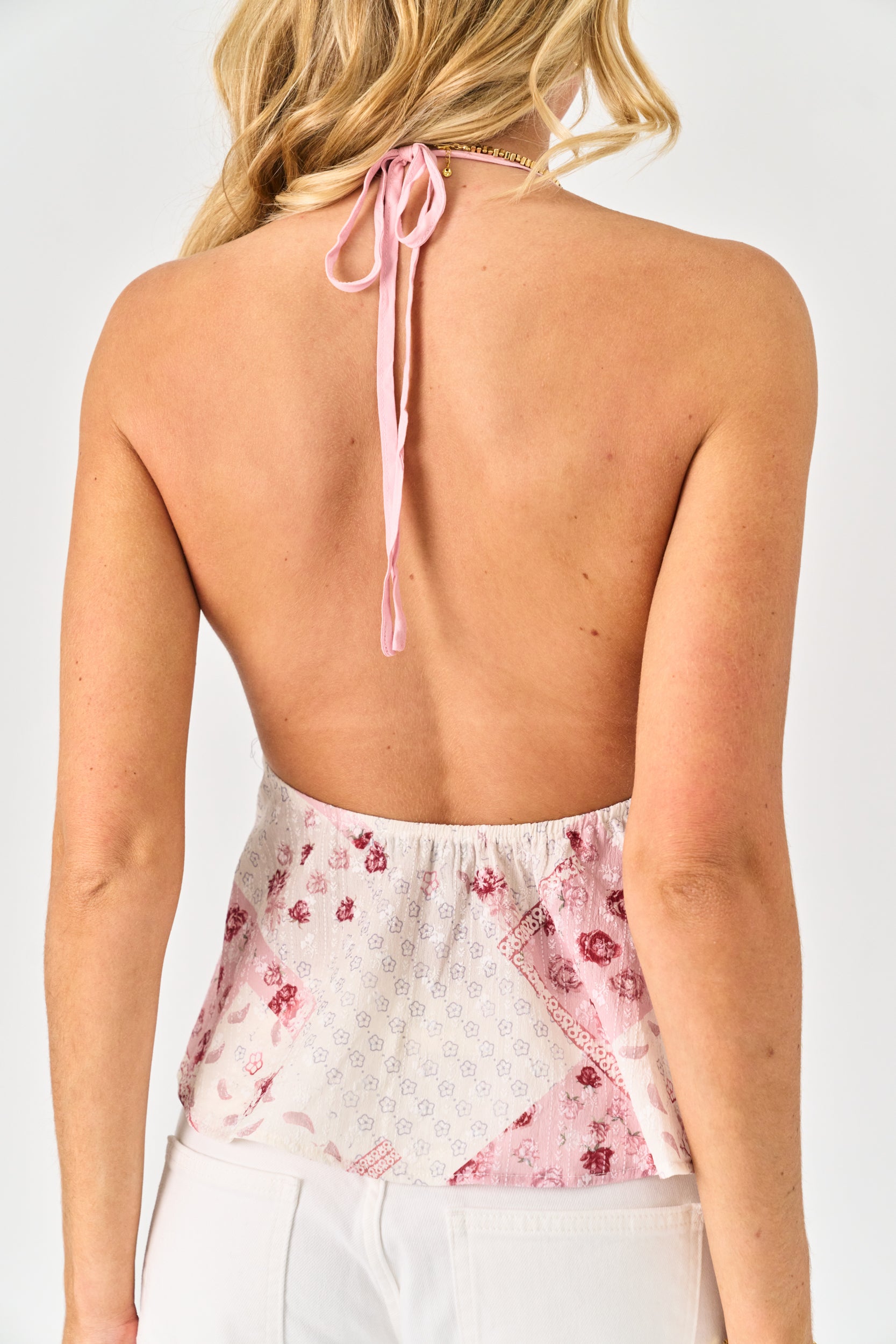 Woman wearing a floral top with an open back and pink straps on a white background
