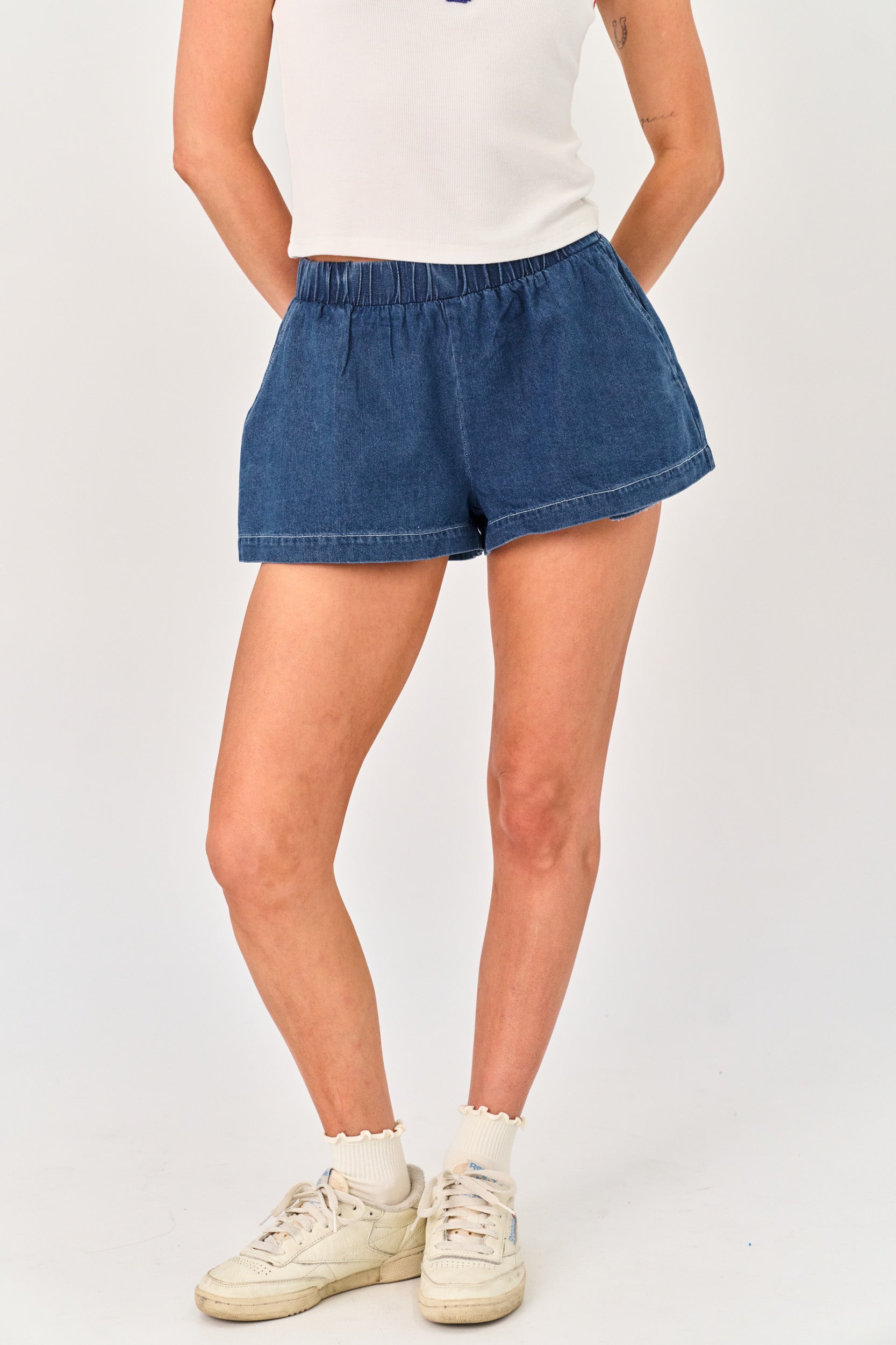 Person wearing blue denim shorts and white sneakers on a plain background