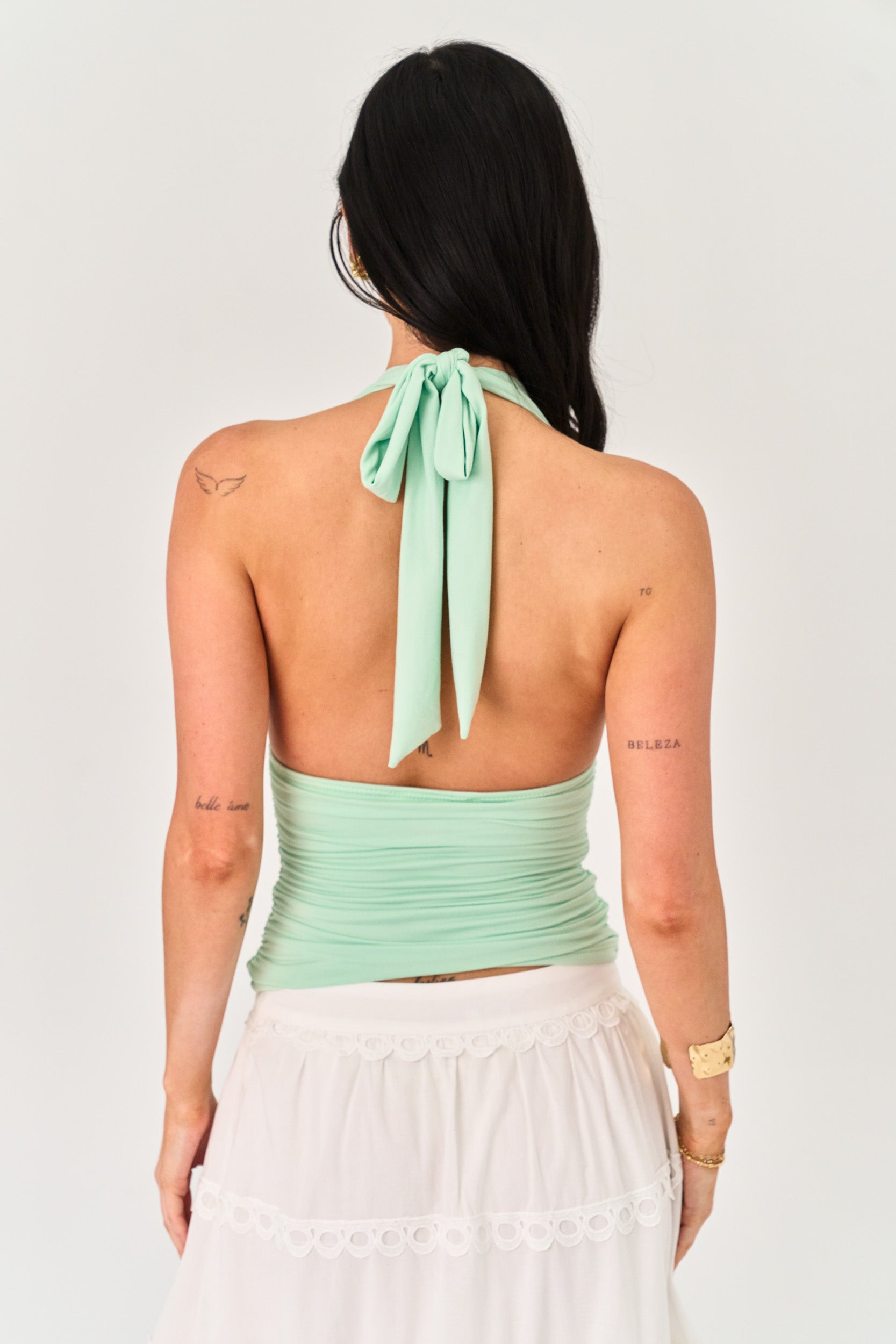 Woman wearing a light green halter top with a tie detail on a white background
