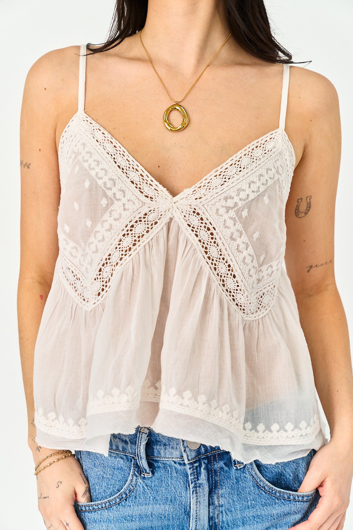 Woman wearing a white lace-trimmed top and blue jeans on a plain background