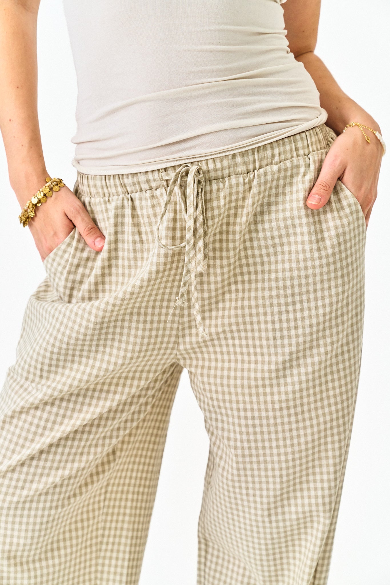 Person wearing beige checkered pants and a white top on a white background