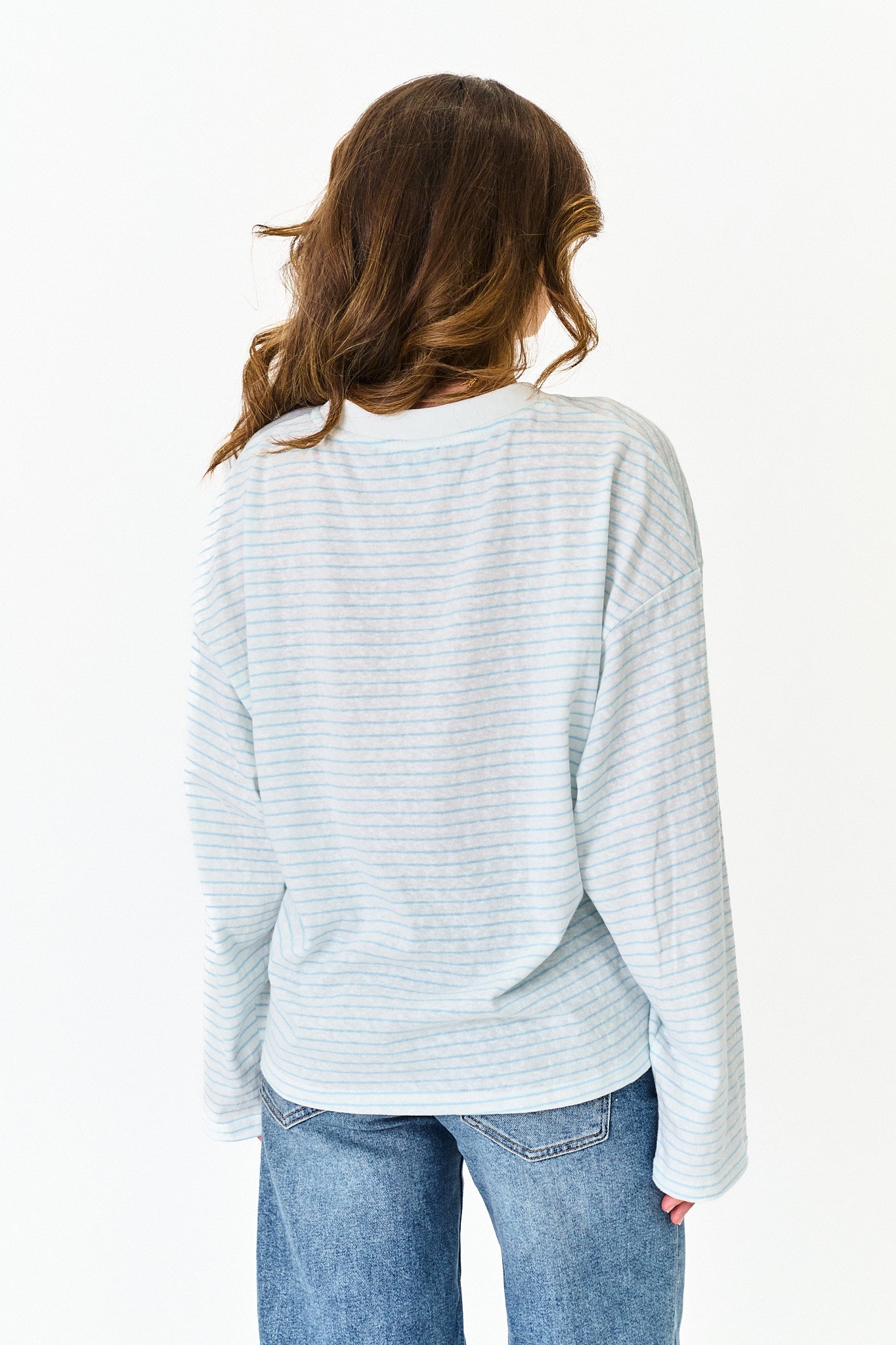 Person wearing a light blue striped sweater and jeans on a white background