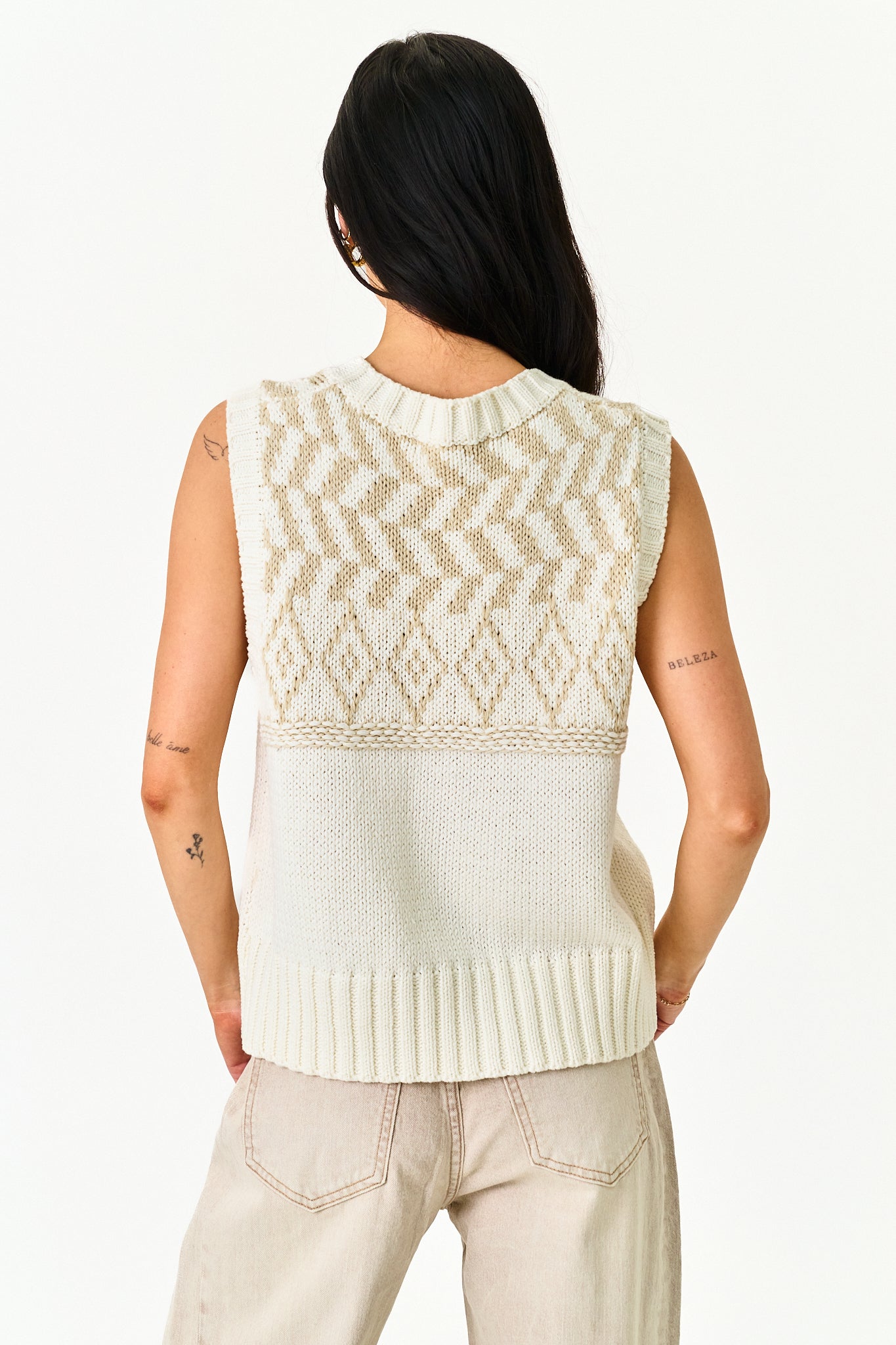 A woman shown from the back wearing a sleeveless knit sweater vest with a cream and beige geometric pattern, paired with light beige pants, against a plain white background.