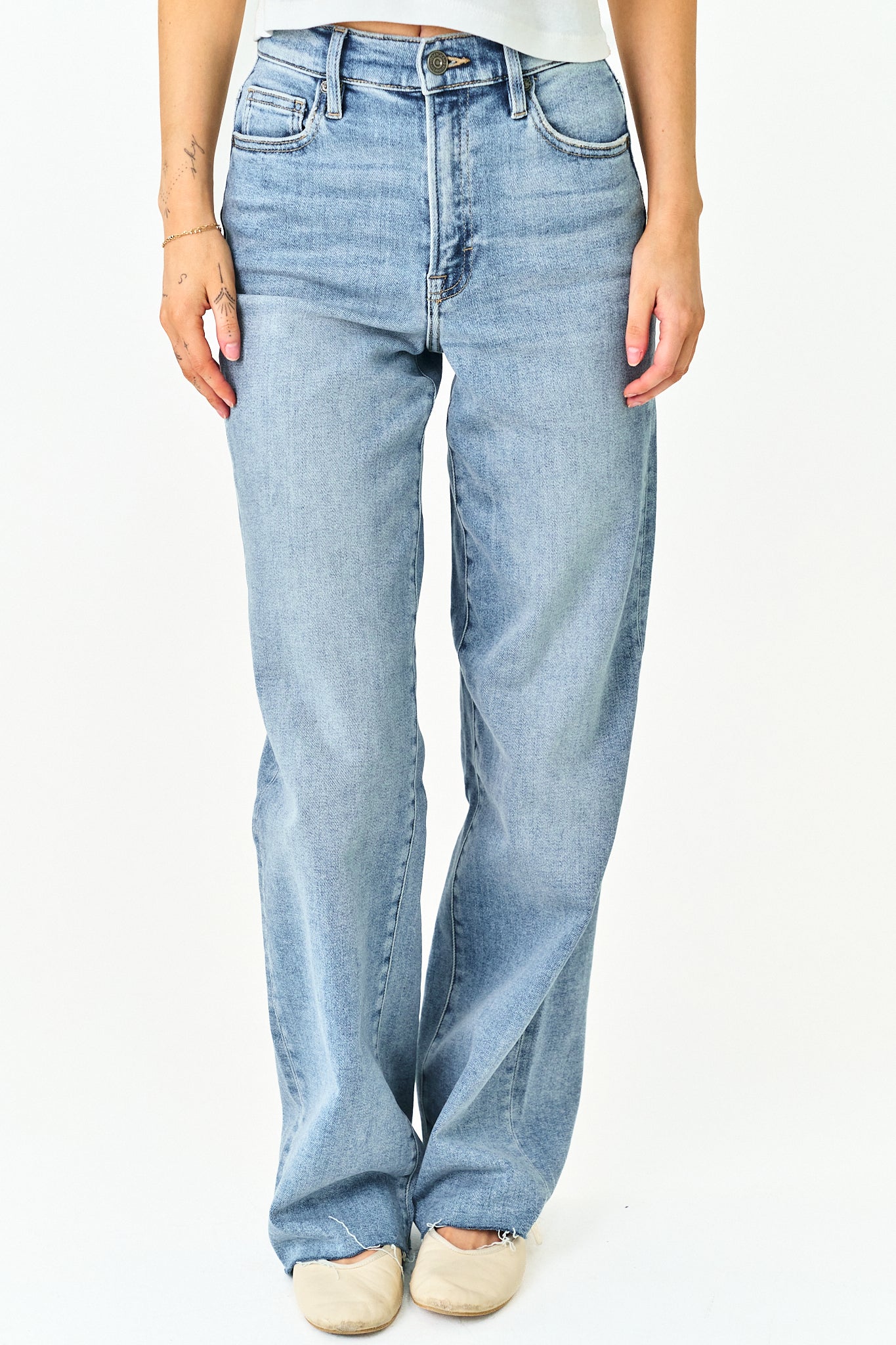 A person wearing light-wash blue denim jeans with a straight-to-wide leg fit, paired with a white top and beige shoes, shown against a plain white background.