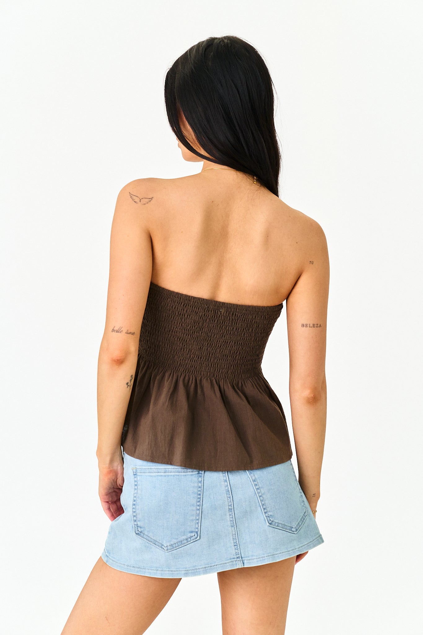 A woman shown from the back wearing a dark brown strapless smocked peplum top and a light blue denim mini skirt, against a plain white background.