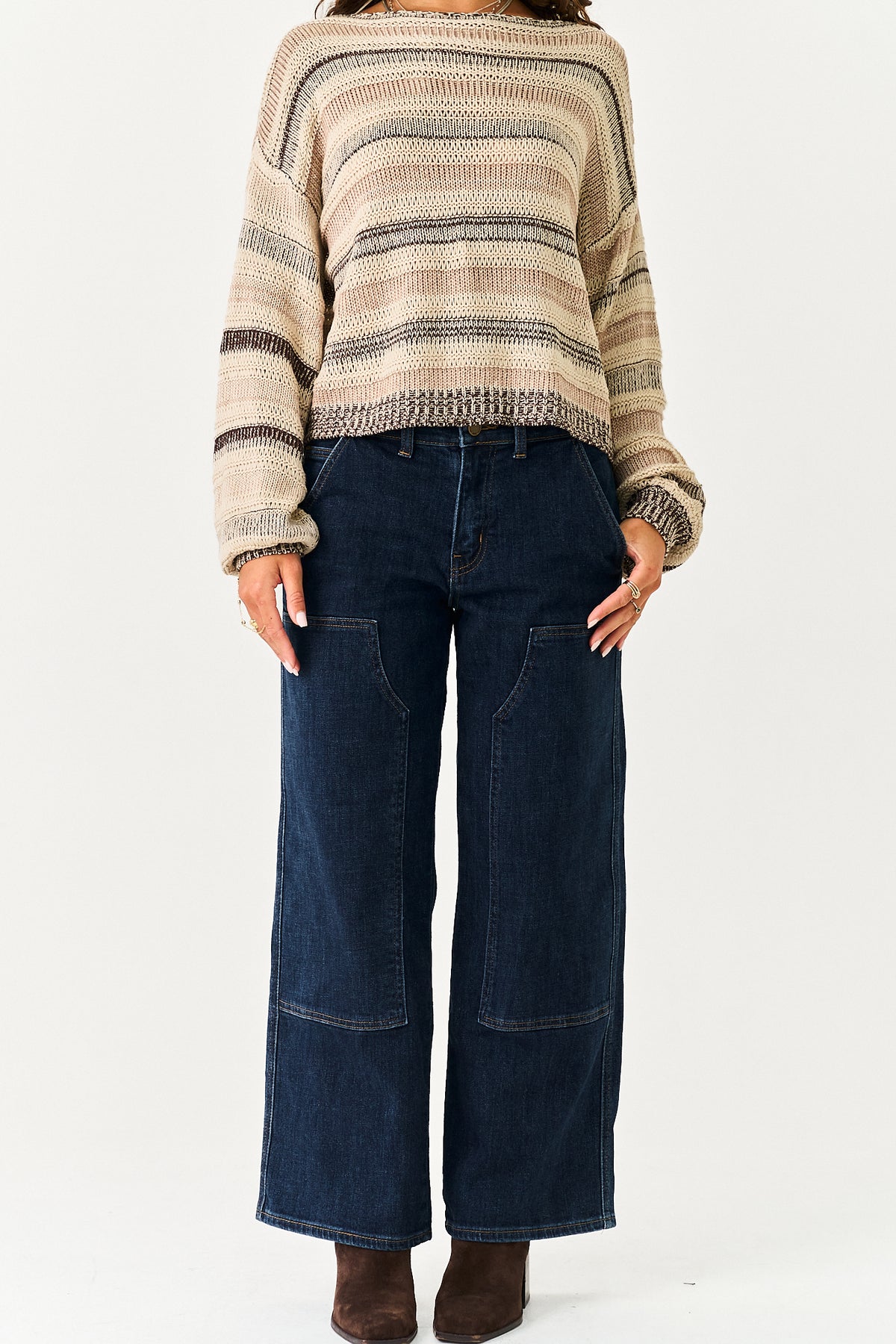 A model wearing a beige and brown striped knit sweater with dark blue wide-leg denim pants and brown boots, shown from the neck down against a plain white background.