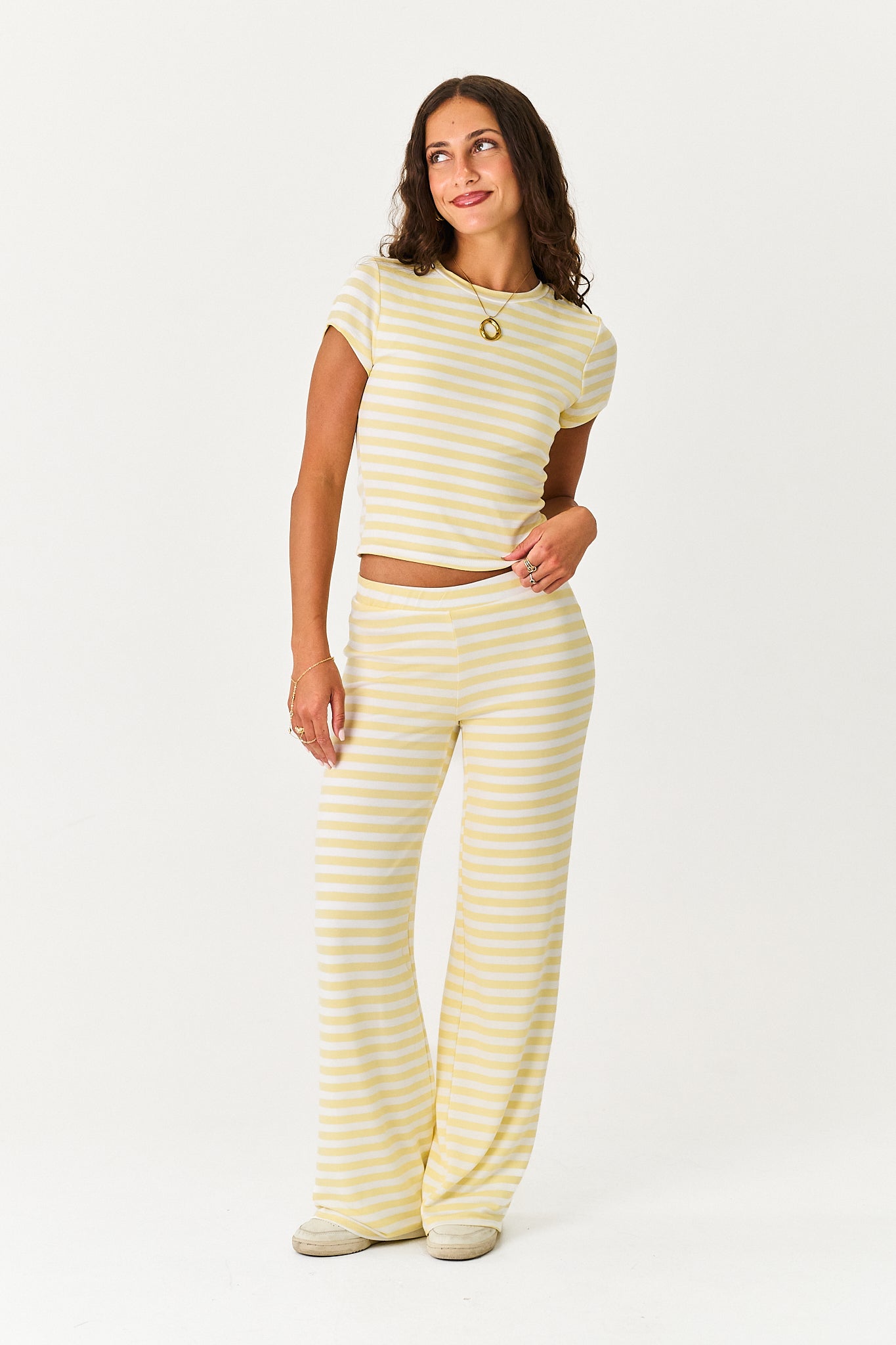 A woman modeling a matching two-piece loungewear set consisting of a short-sleeve cropped top and wide-leg pants, both in a pale yellow and white horizontal stripe pattern, against a plain white studio background.
