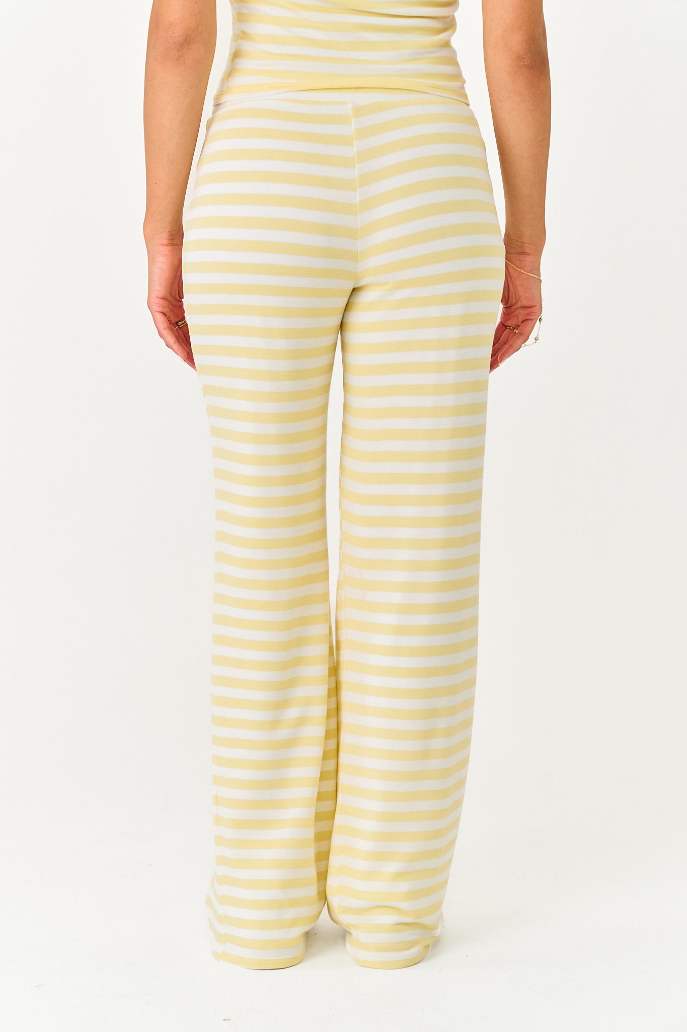 A person shown from the back wearing pale yellow and white horizontally striped wide-leg pants against a plain white studio background.