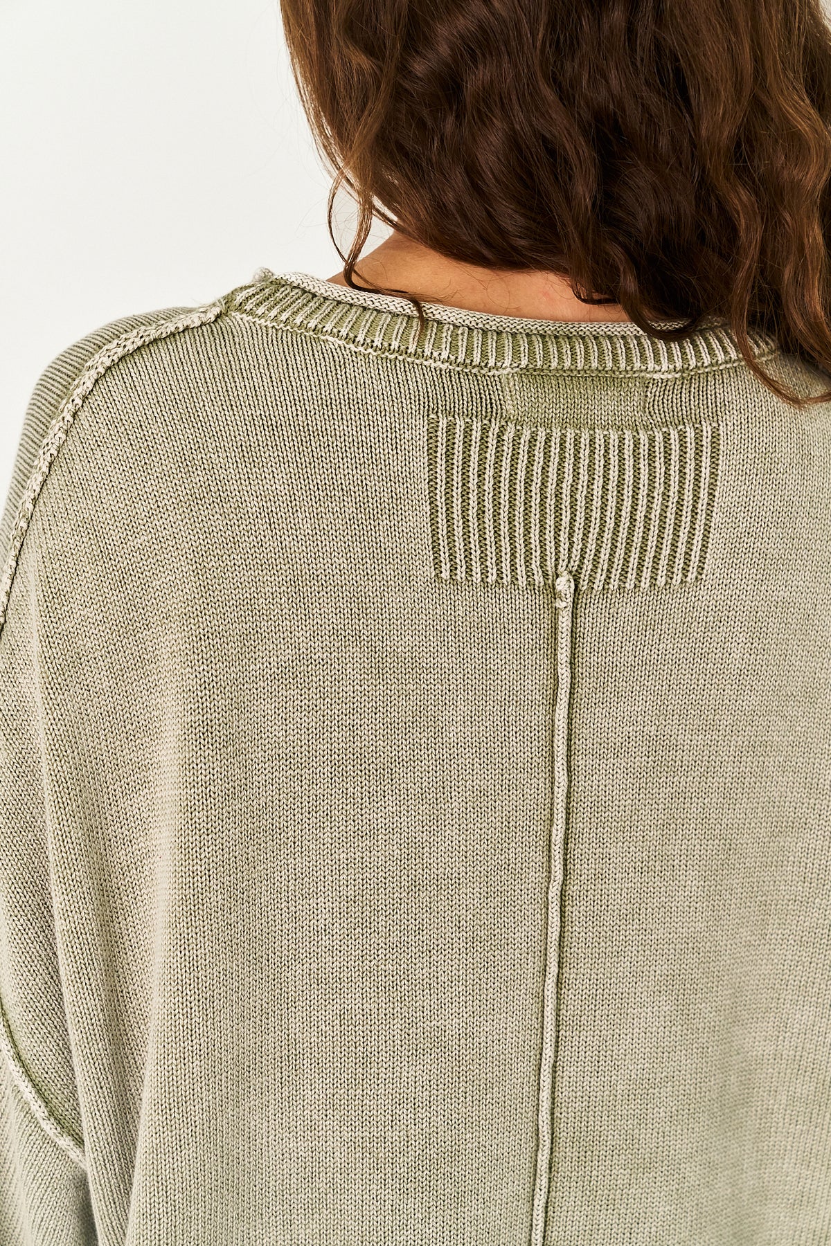 Close-up back view of a person wearing a light sage green knit sweater, showing the ribbed crew neck and a vertical seam detail.