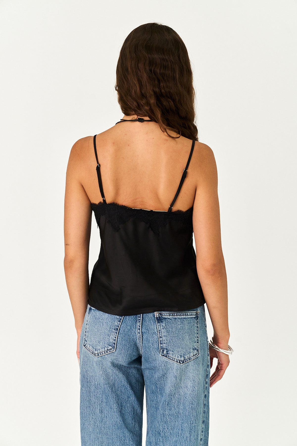 A woman shown from the back wearing a black spaghetti-strap camisole top and light blue jeans against a plain white studio background.