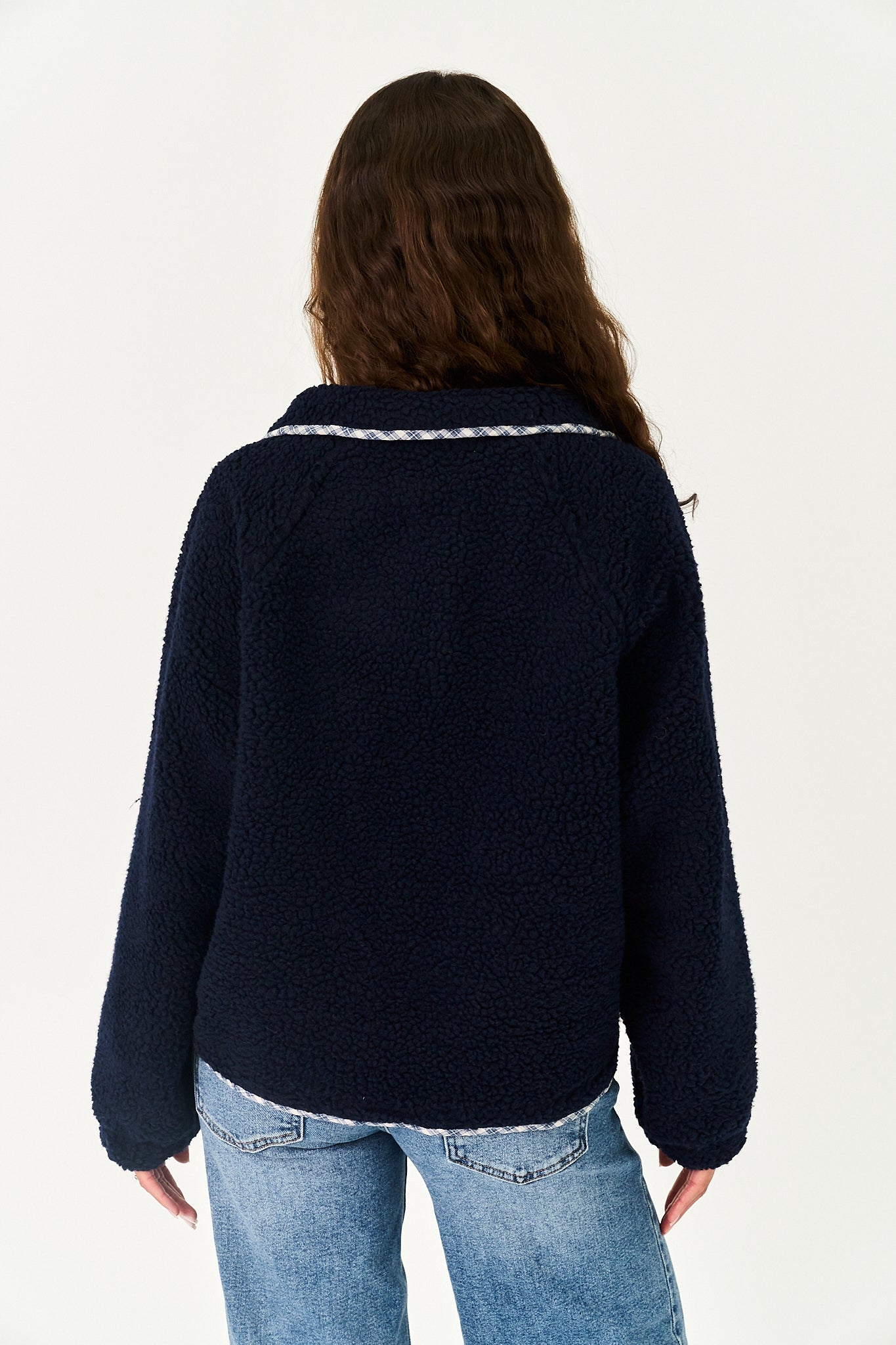 A woman viewed from the back wearing a dark navy blue sherpa fleece jacket with a white textured trim along the collar, paired with light blue jeans, against a plain white background.