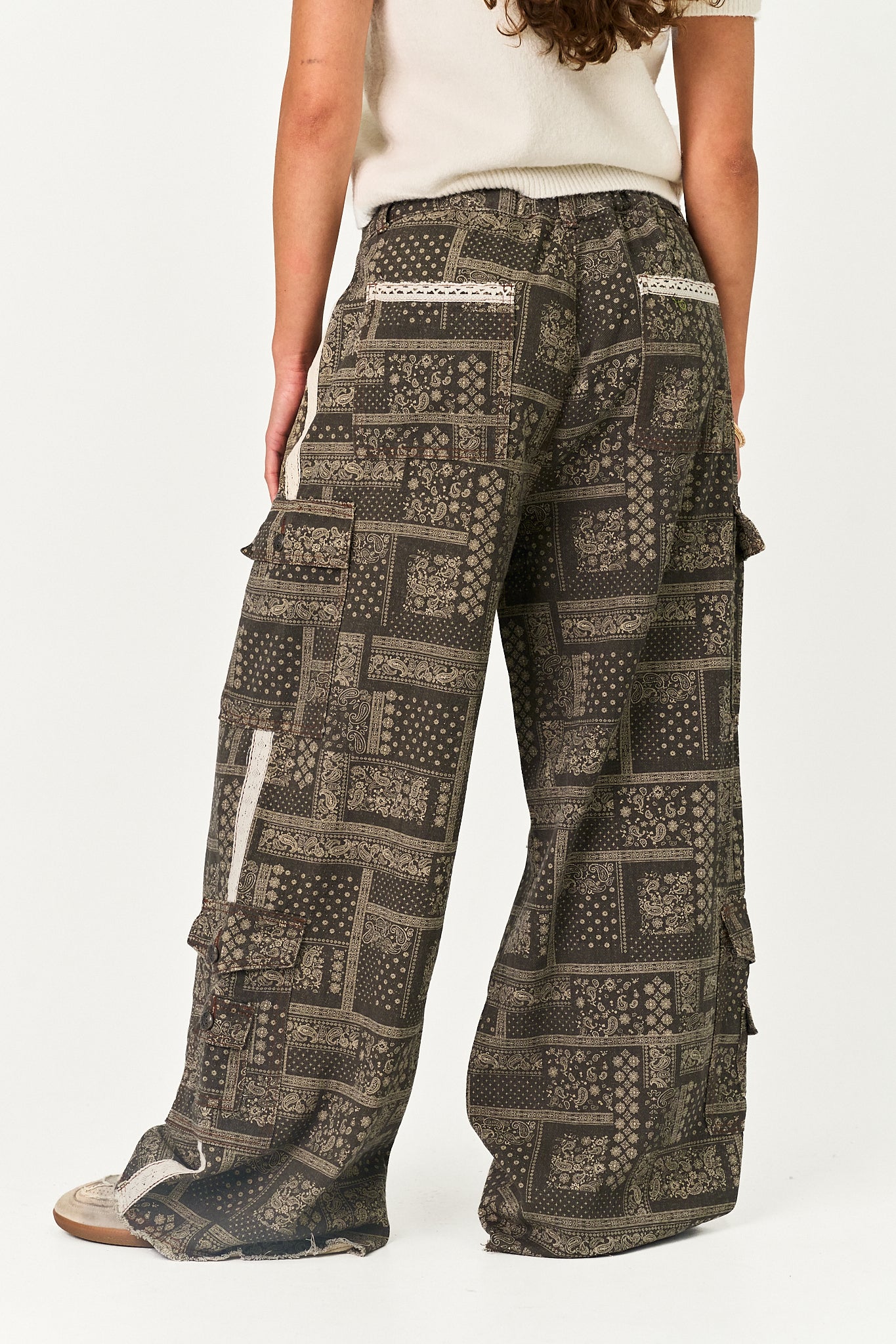 Wide-leg cargo pants with a dark brown and beige bandana print, shown on a model from the back against a white studio background.