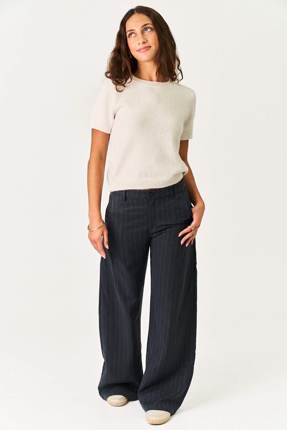 A woman modeling a short-sleeve cream knit top and dark navy wide-leg pinstripe trousers against a plain white studio background.
