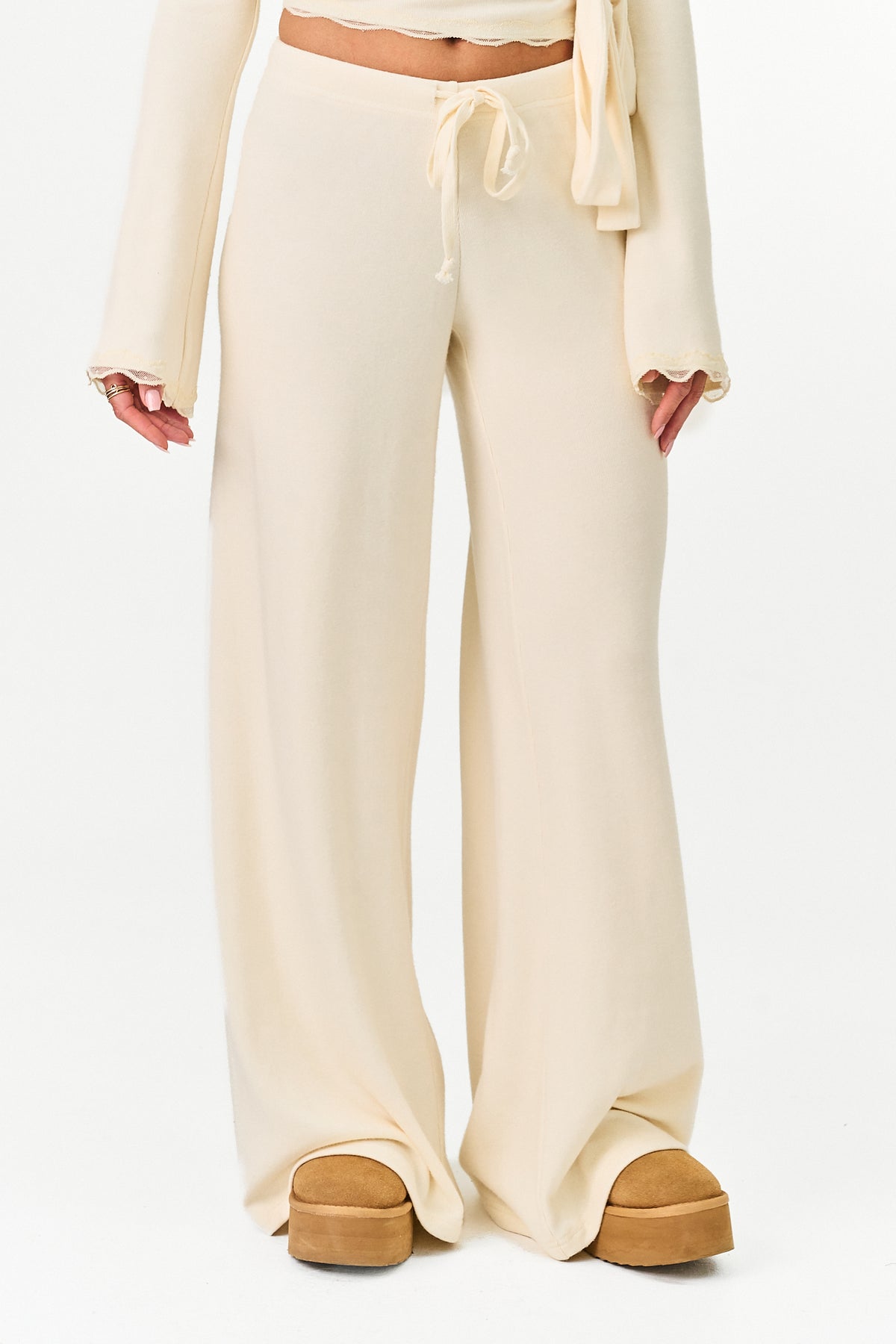 Cream wide-leg lounge pants with a drawstring waist, shown on a model wearing tan platform shoes against a plain white background.