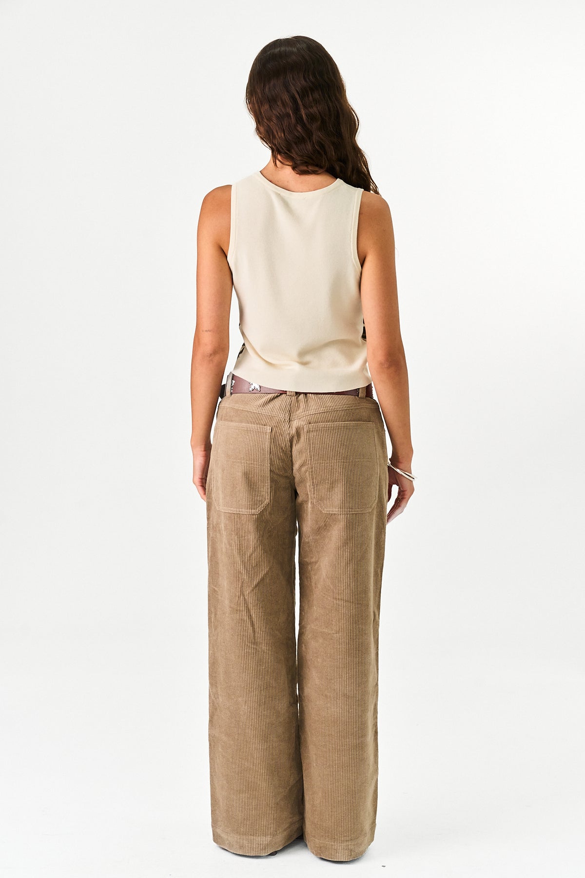 A woman shown from the back wearing a cream sleeveless top and wide-leg tan pants against a plain white studio background.