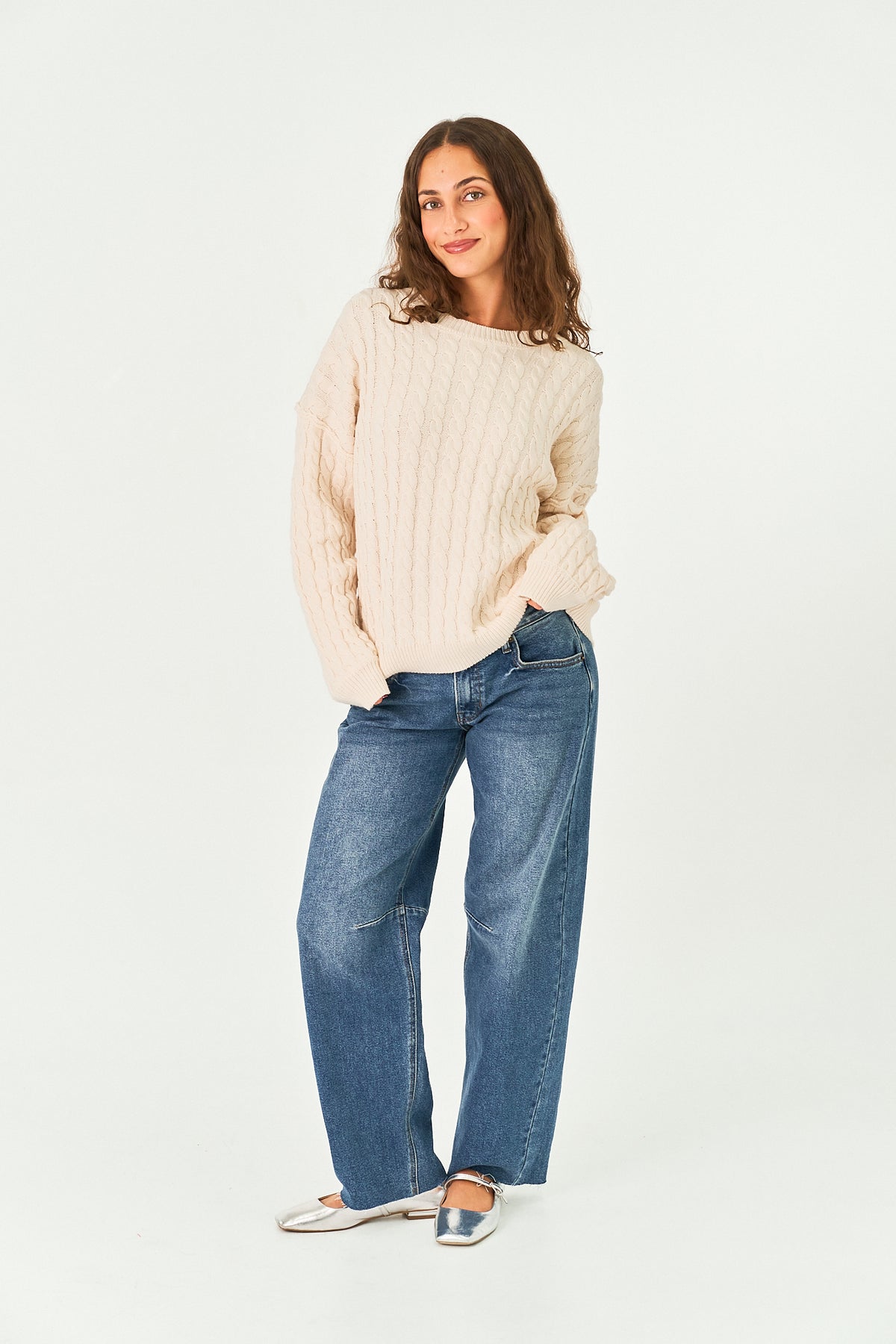 A woman modeling a cream ribbed knit sweater and wide-leg blue jeans against a plain white studio background.