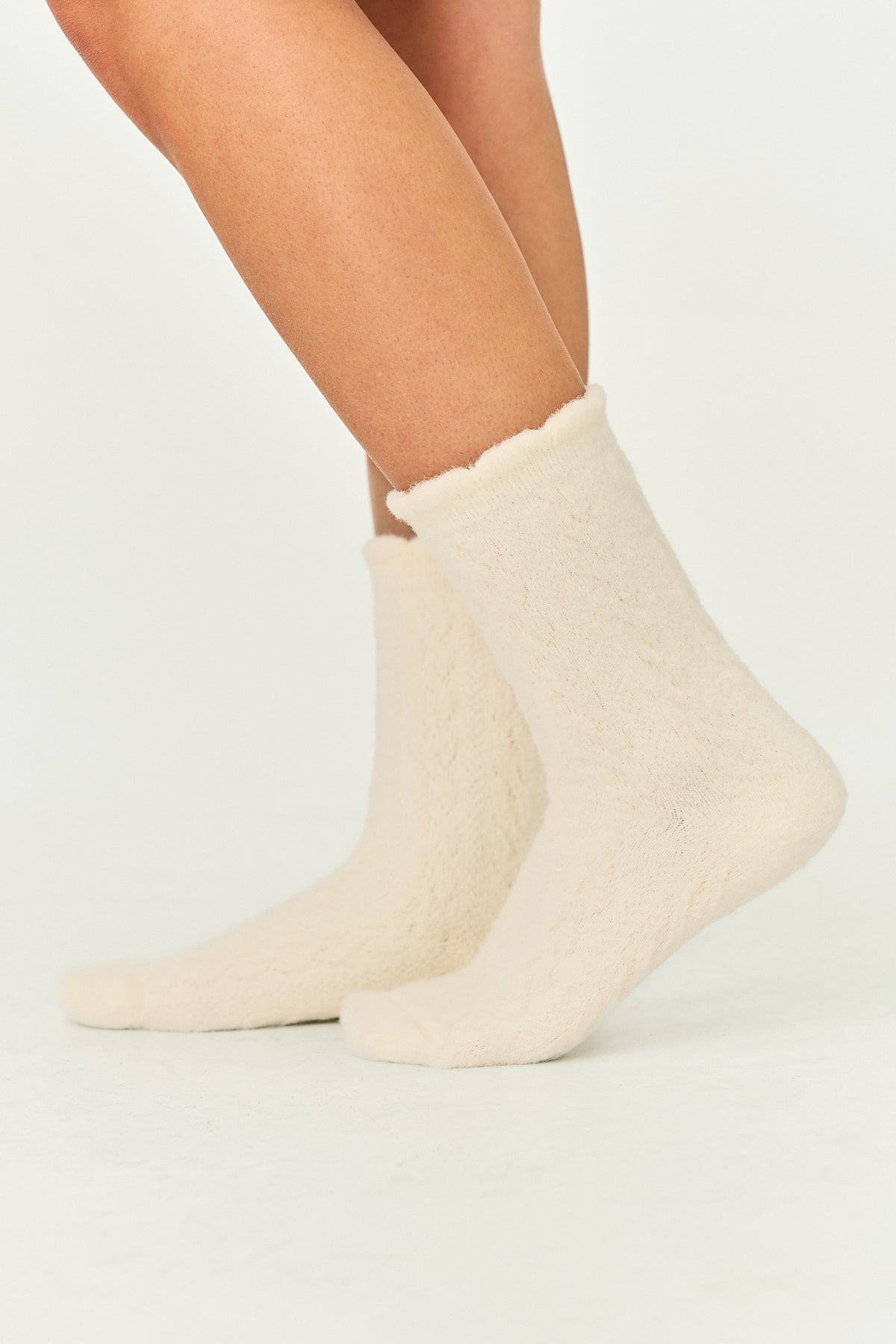 A pair of cream-colored, textured plush crew socks worn on a person's feet, shown against a plain light background.