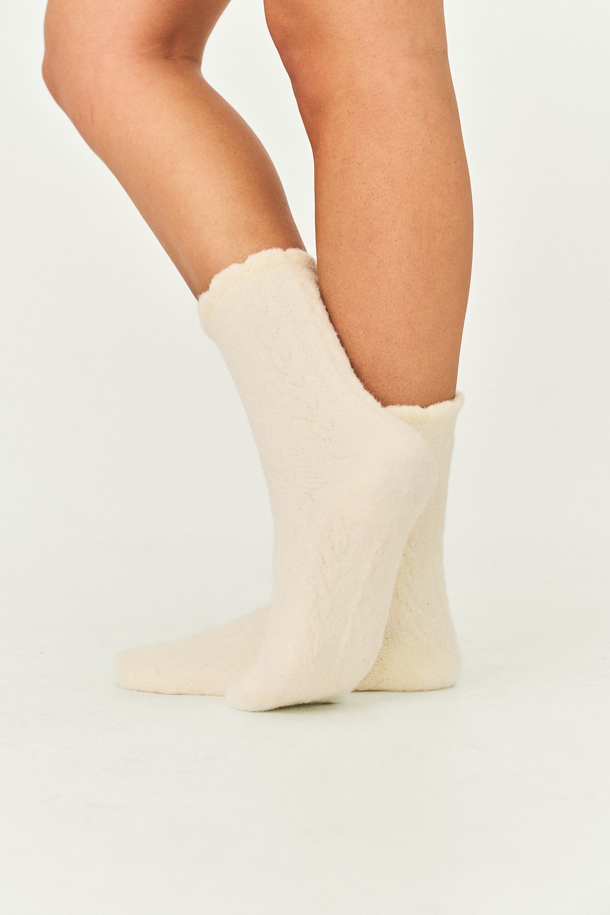 A pair of cream-colored, plush fuzzy ankle socks worn on a person's feet, shown against a plain white studio background.