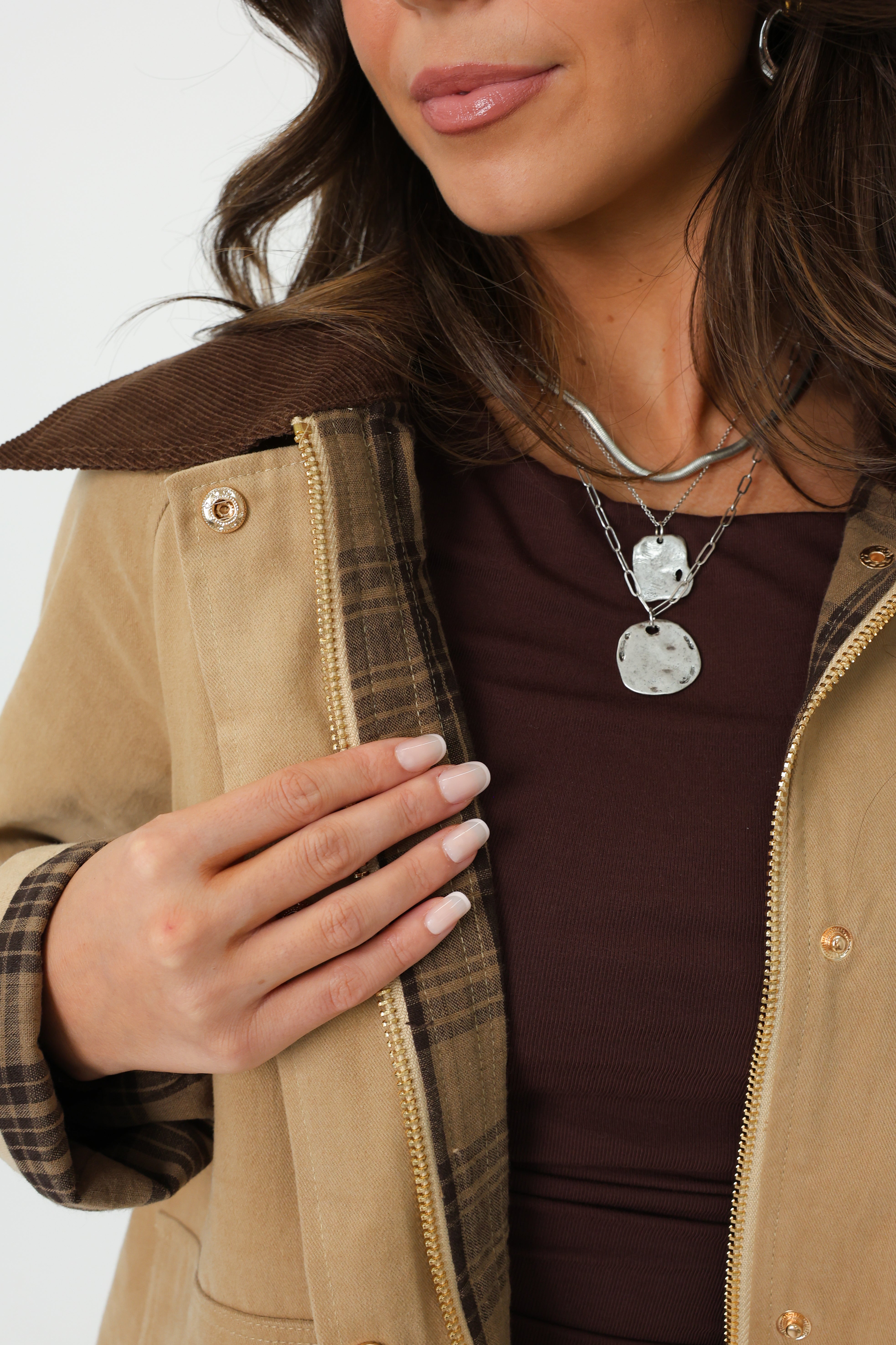 Person wearing a brown jacket with a plaid pattern, holding their hand to their chest.