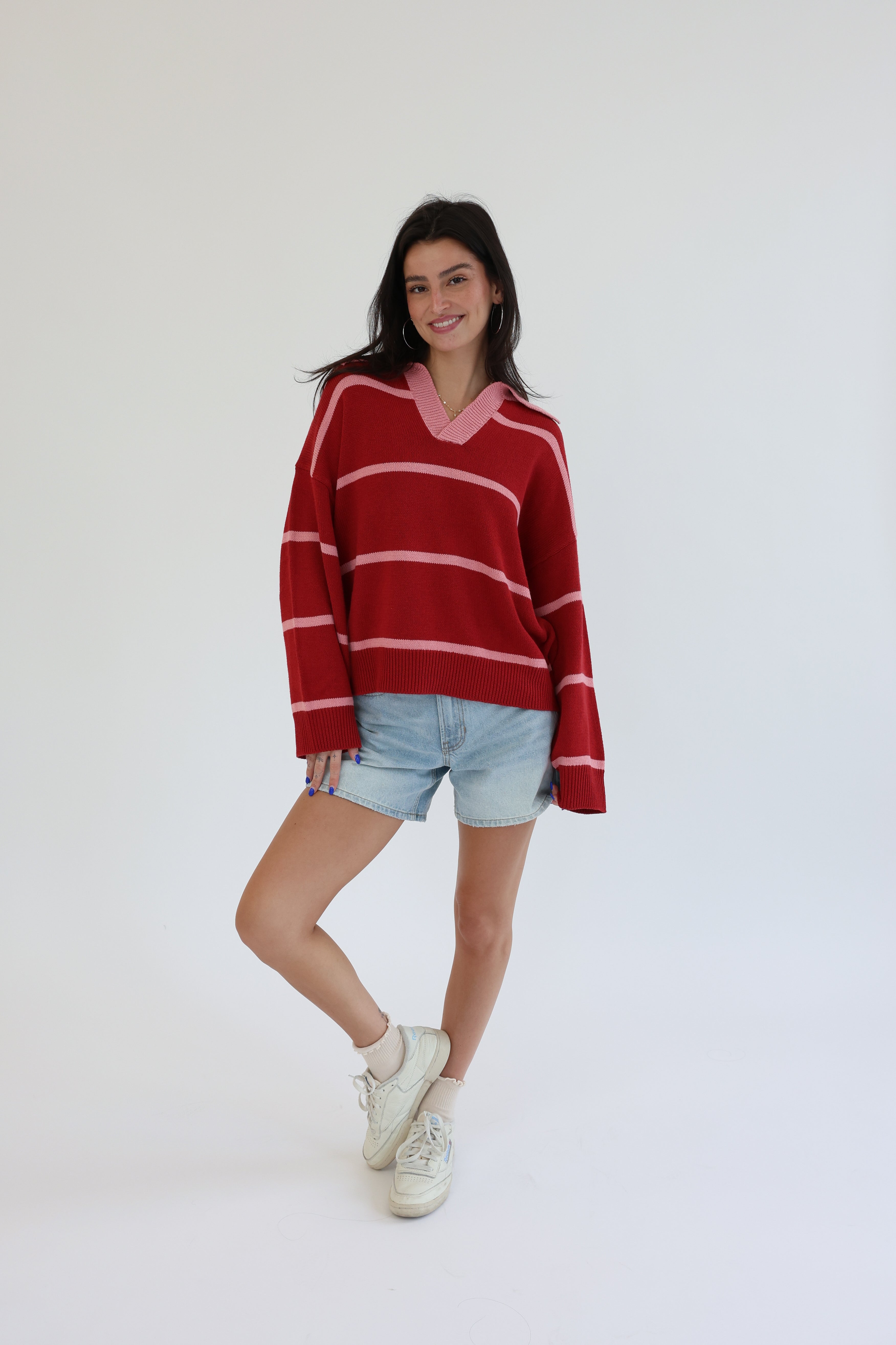 Woman wearing a red and white striped sweater with denim shorts on a white background