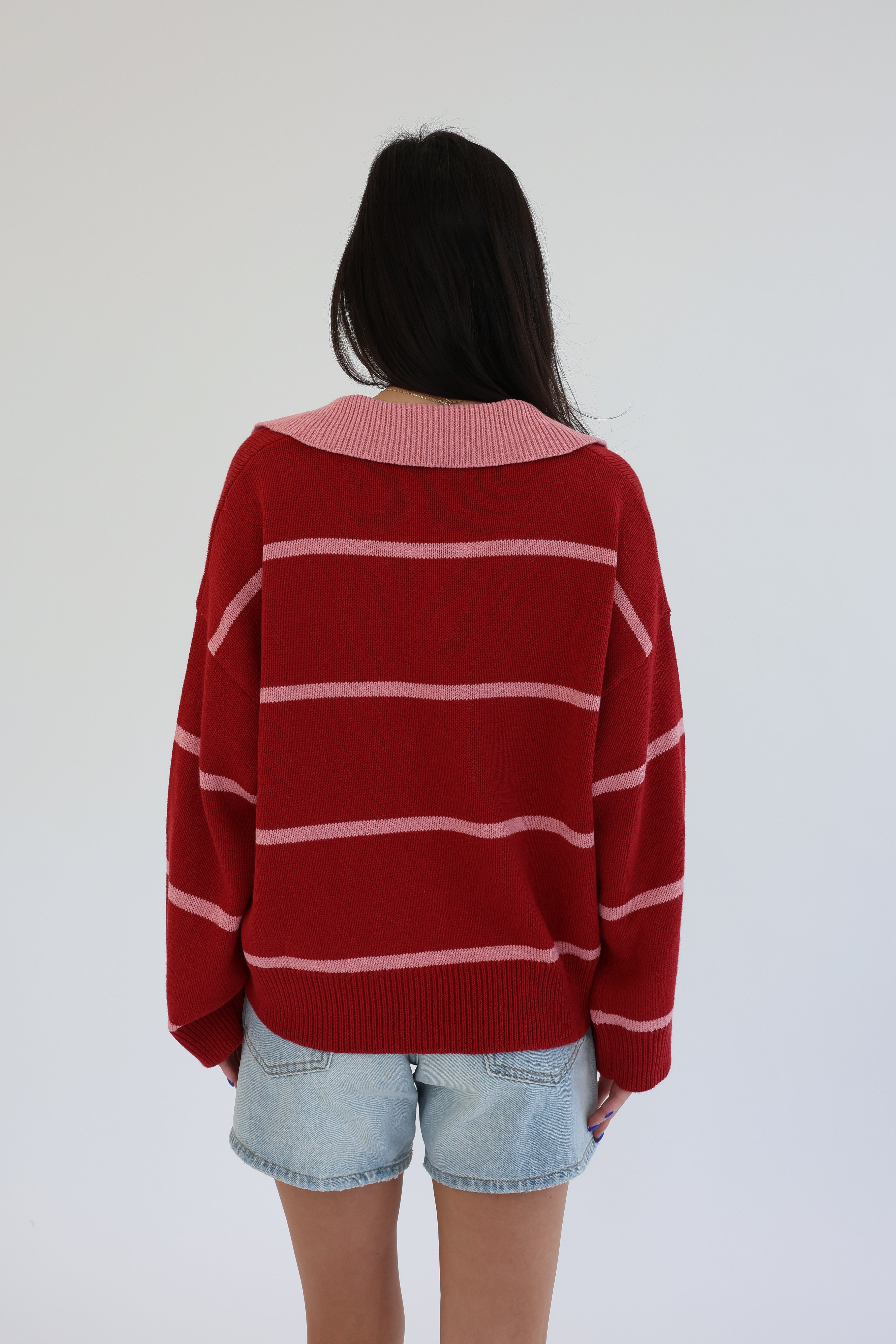 Person wearing a red and white striped sweater with denim shorts on a plain background