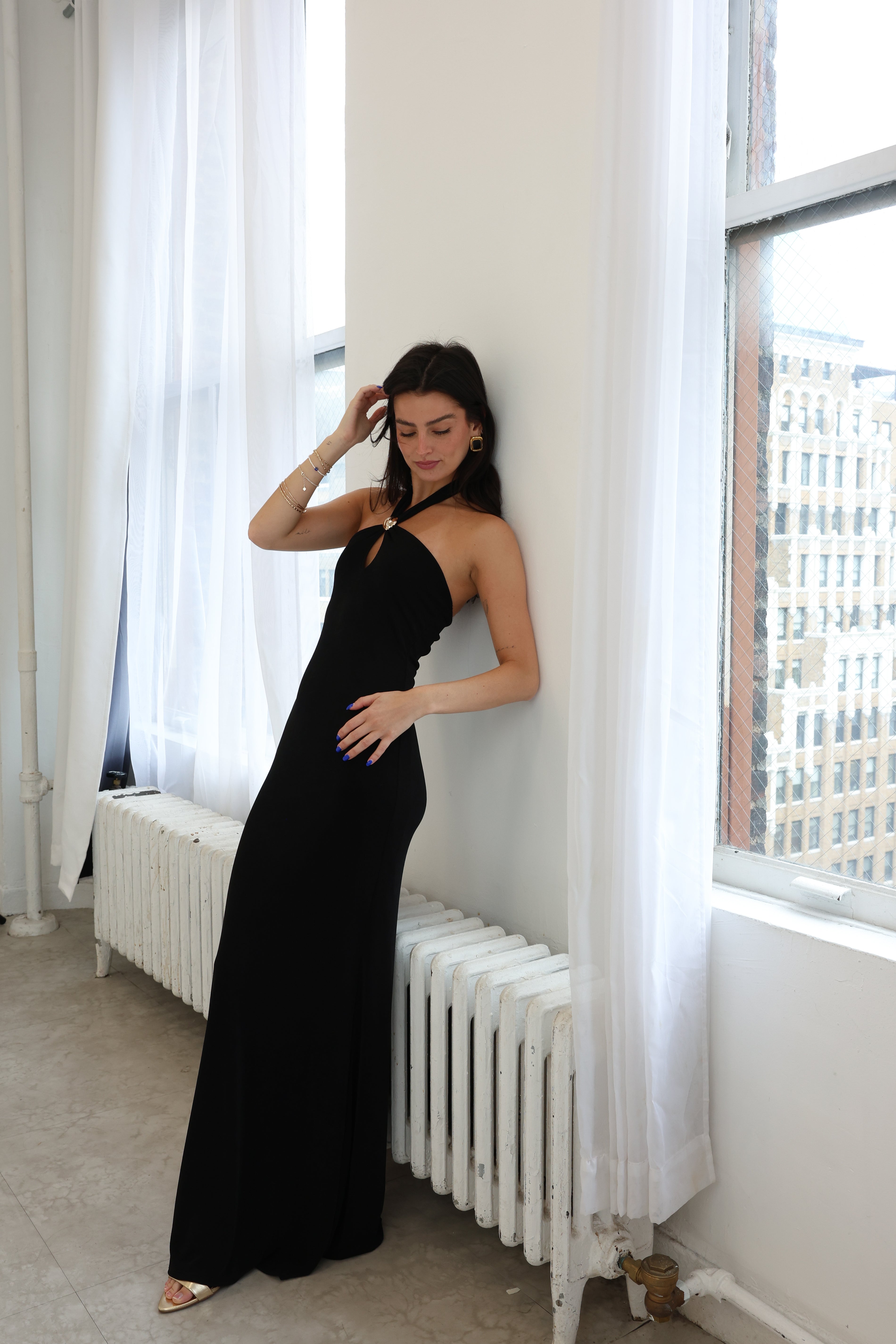 Woman in a black dress standing against a white wall with large windows.