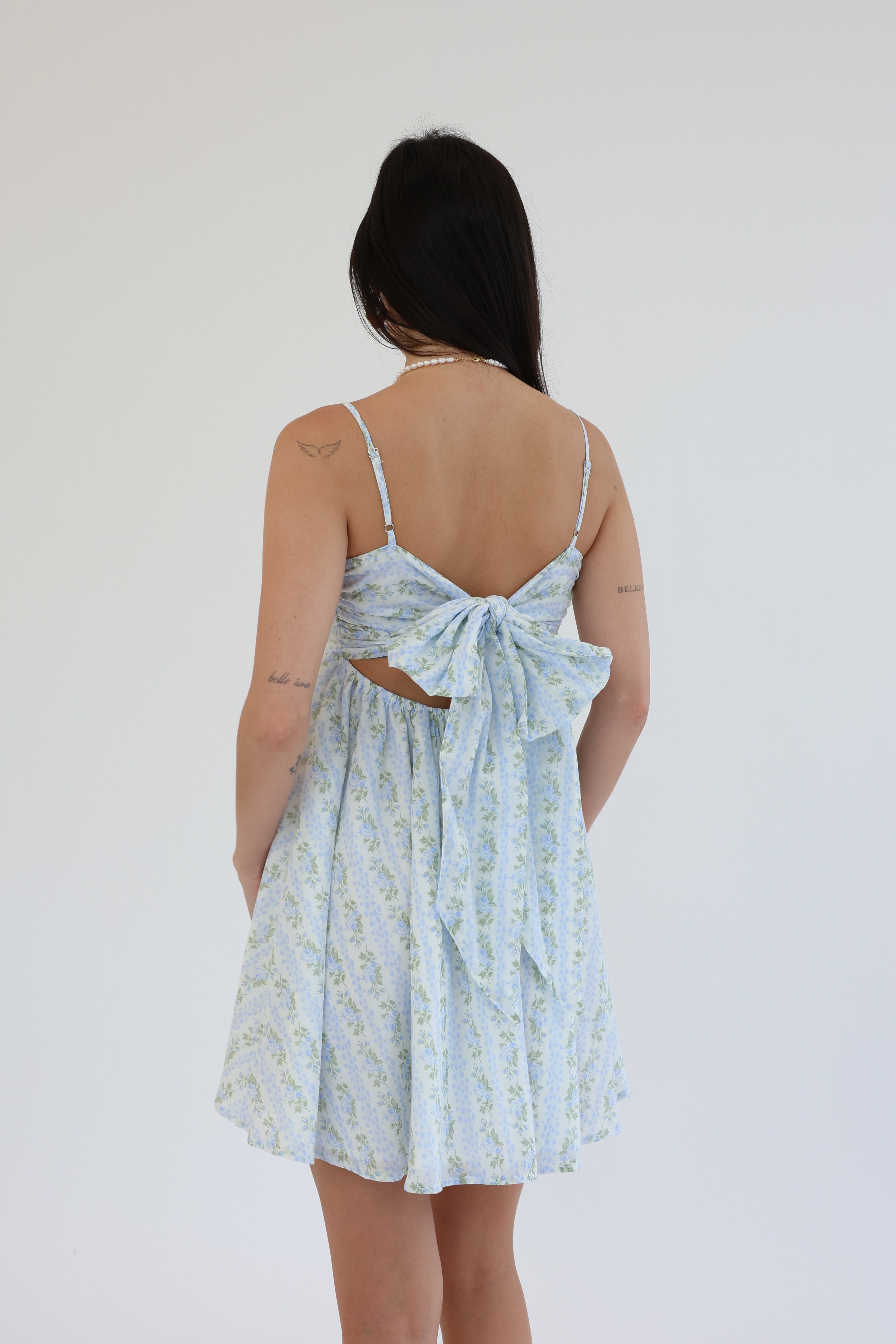 Woman wearing a light blue floral dress with a bow detail on a white background