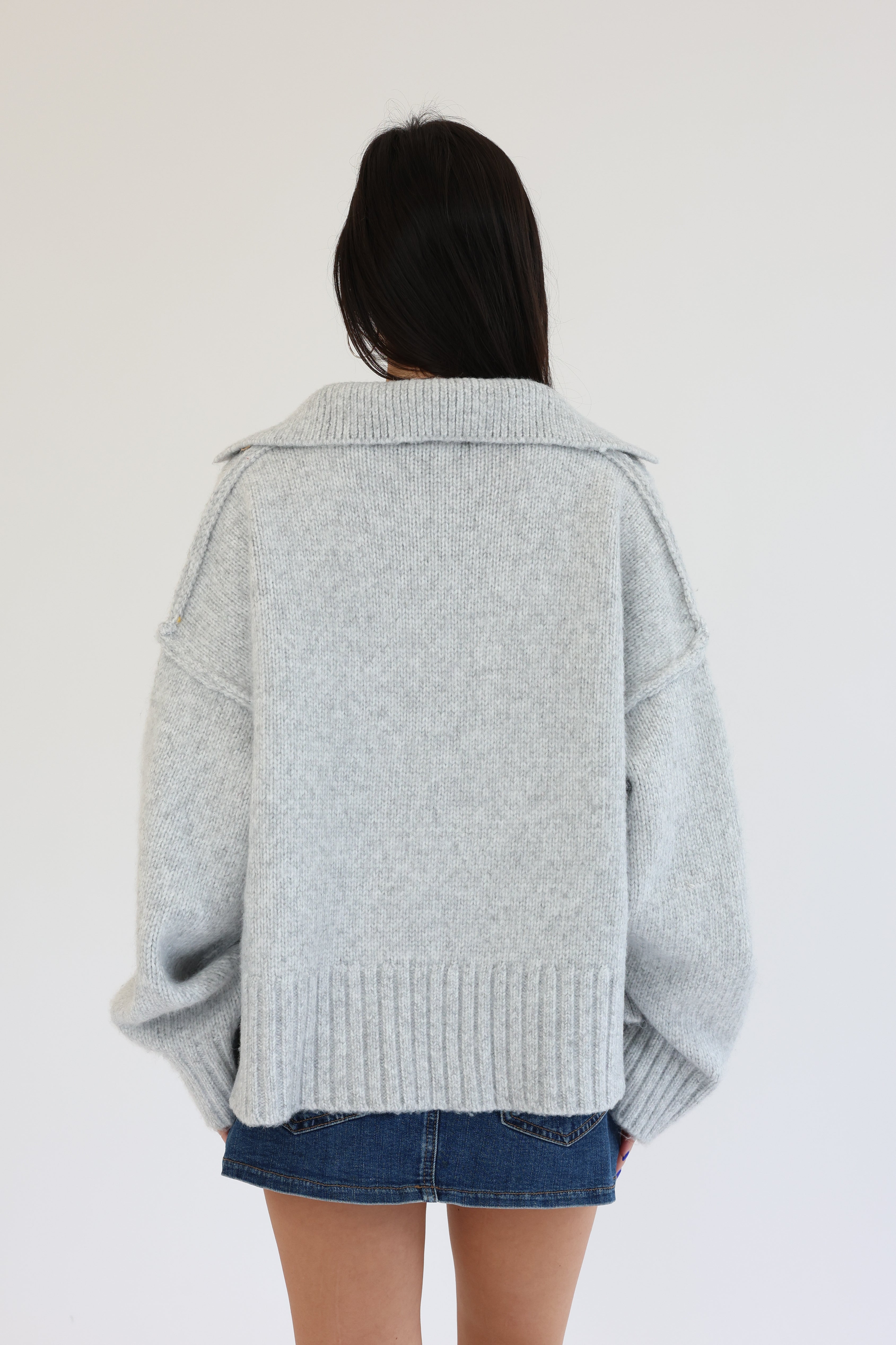 Person wearing a light gray sweater over a denim skirt on a white background