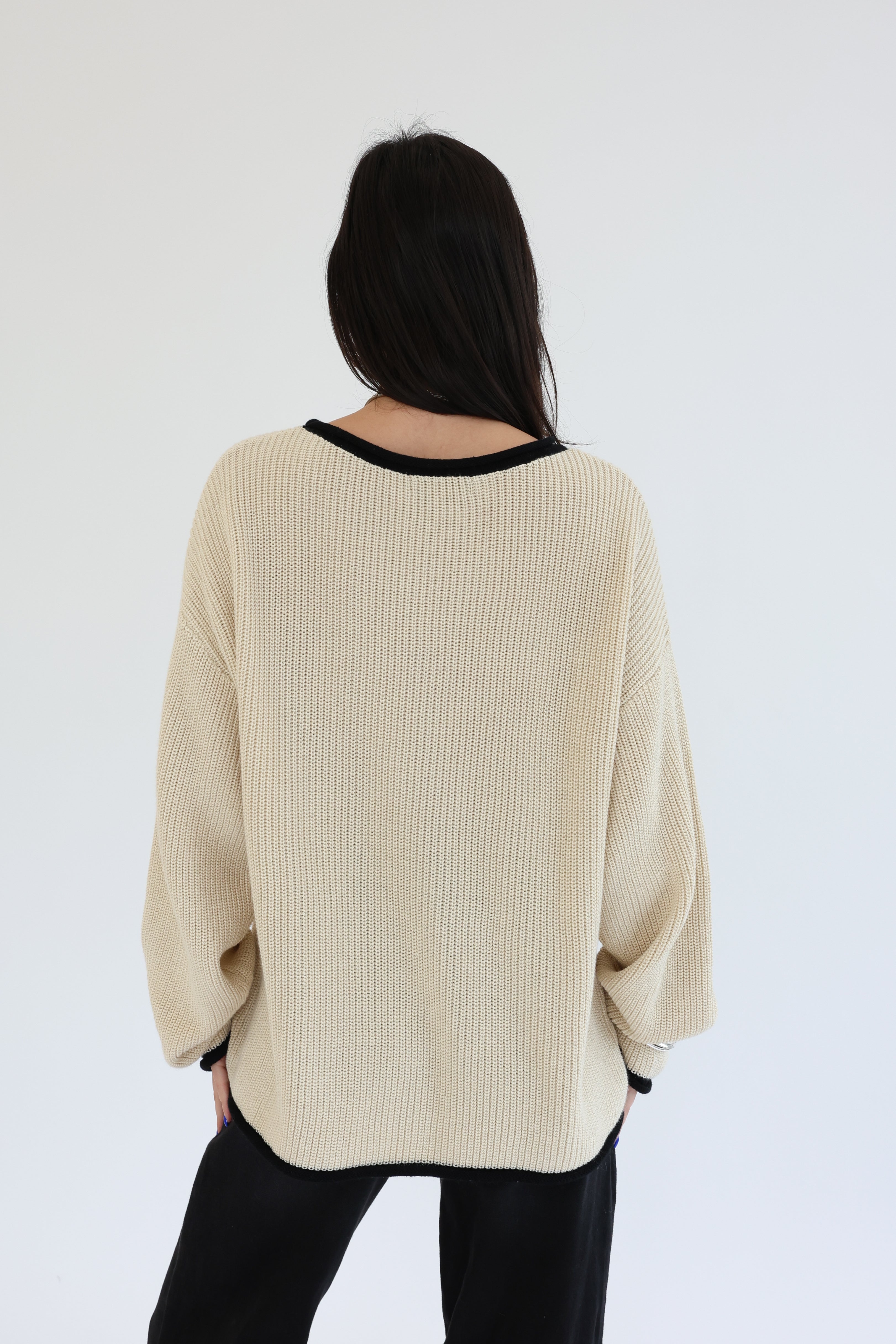Person wearing a beige ribbed sweater with a plain white background