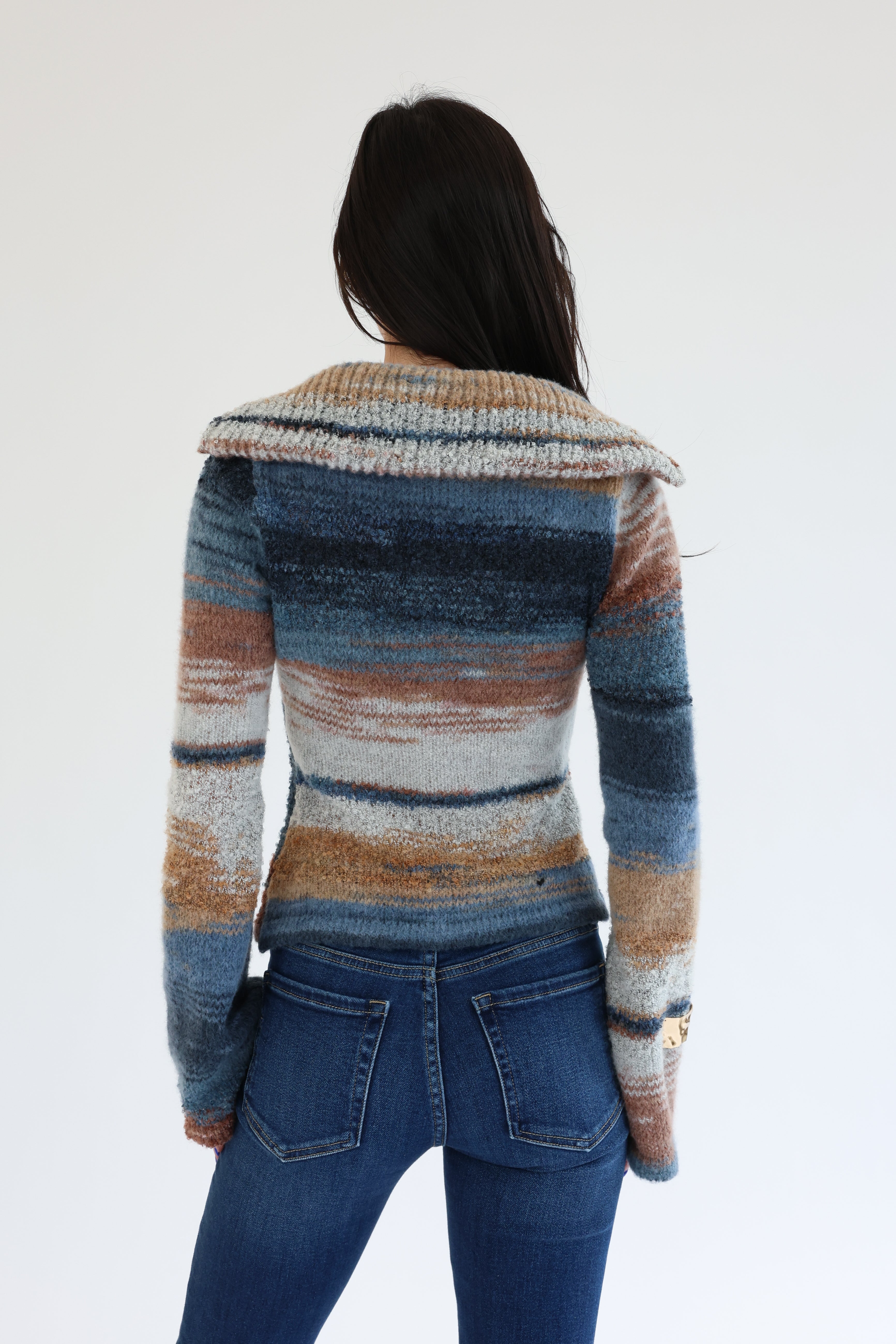 Person wearing a multicolored striped sweater and blue jeans on a white background