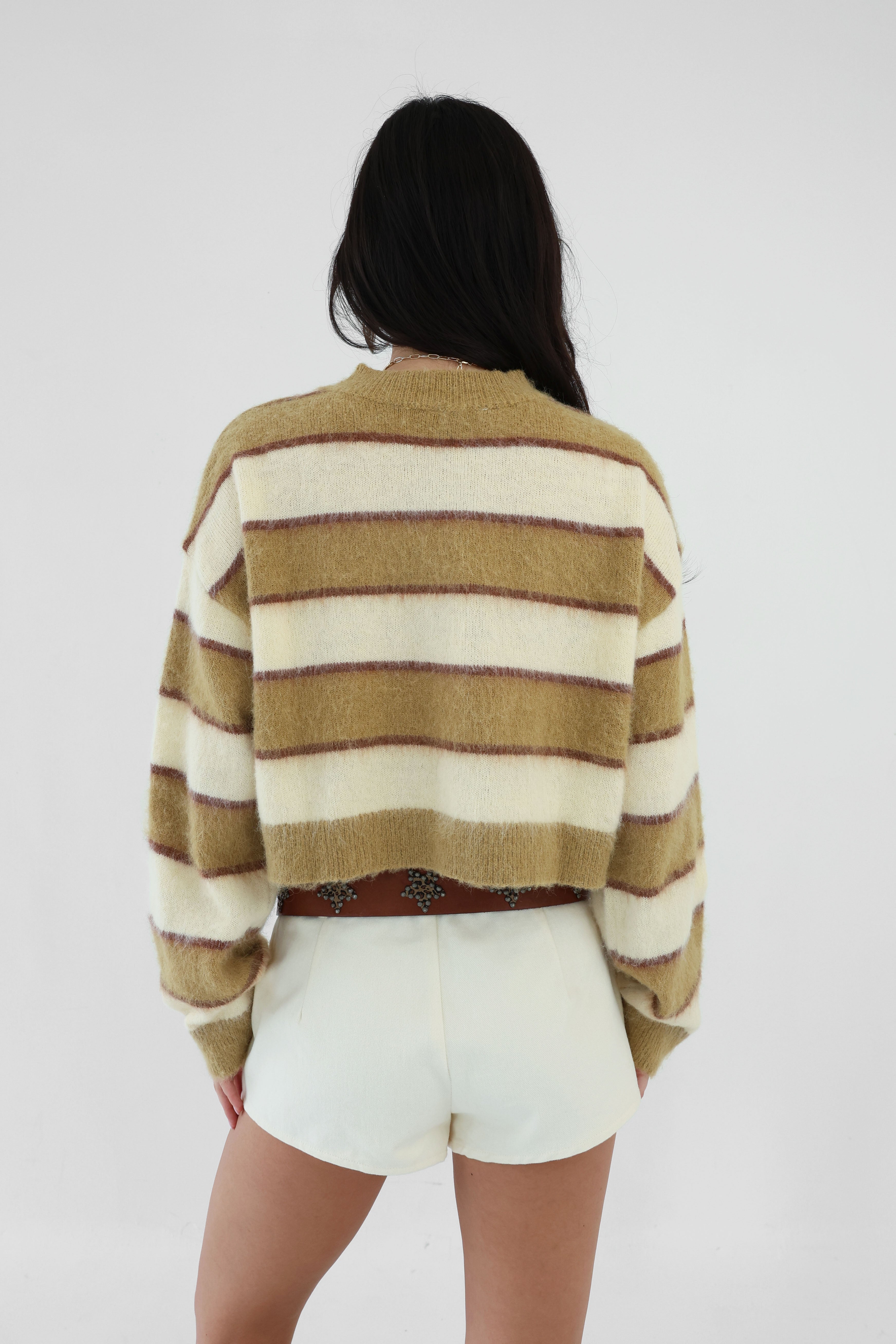 Person wearing a striped sweater and white shorts on a plain background